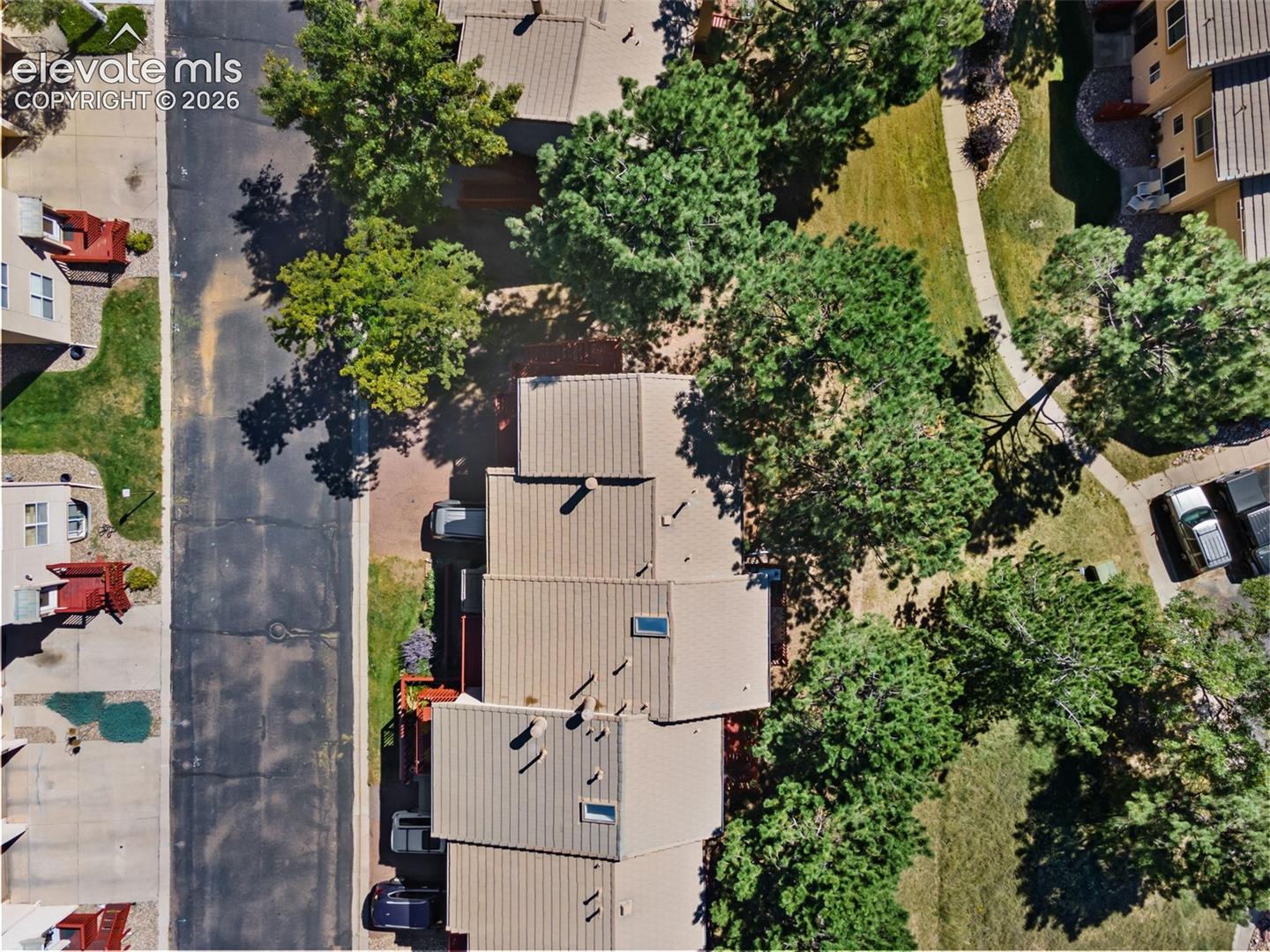 Aerial perspective featuring a metal roof system, integrated skylights, and mature tree canopy, surrounded by established landscaping and paved asphalt surfaces