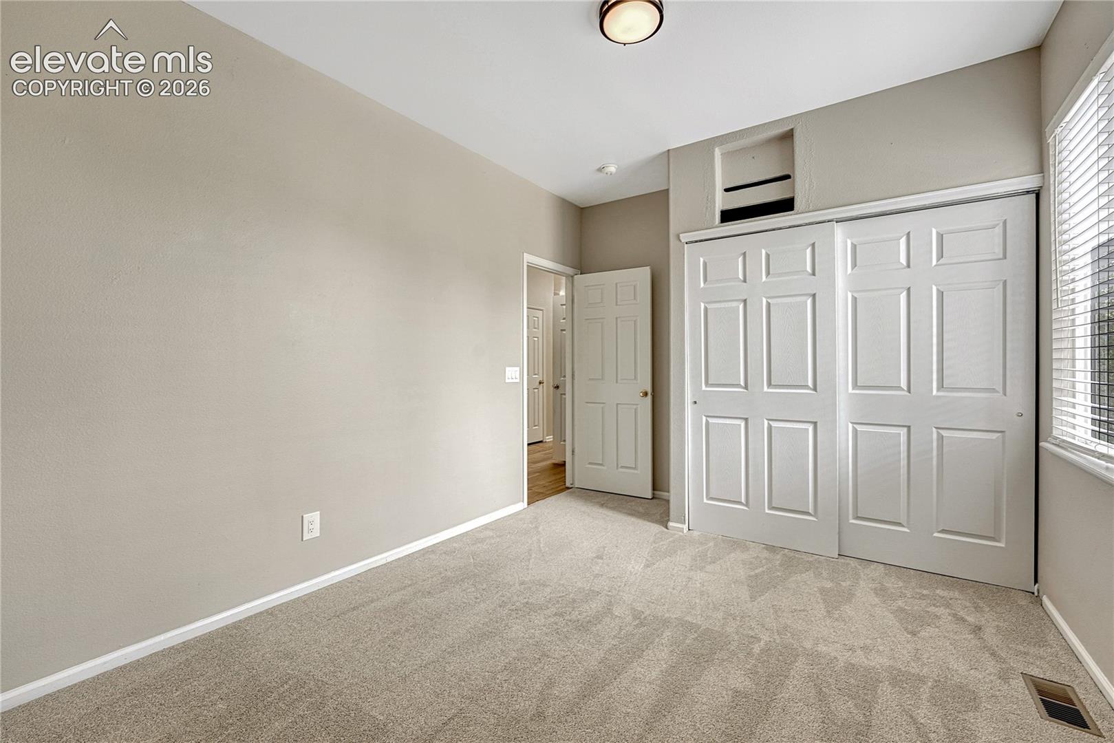 Neutral-toned interior featuring wall-to-wall carpeting, a multi-panel sliding closet door, and a six-panel passage door