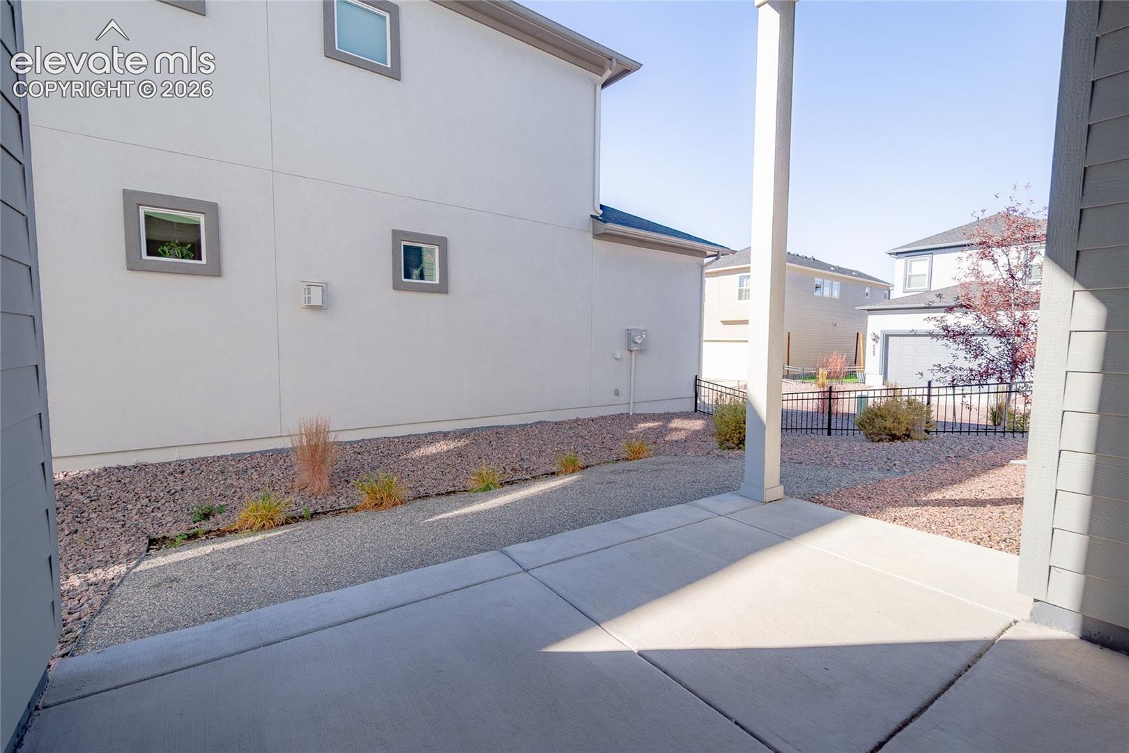 Covered concrete patio with a supporting column, finished with xeriscaping featuring decorative gravel and metal perimeter fencing
