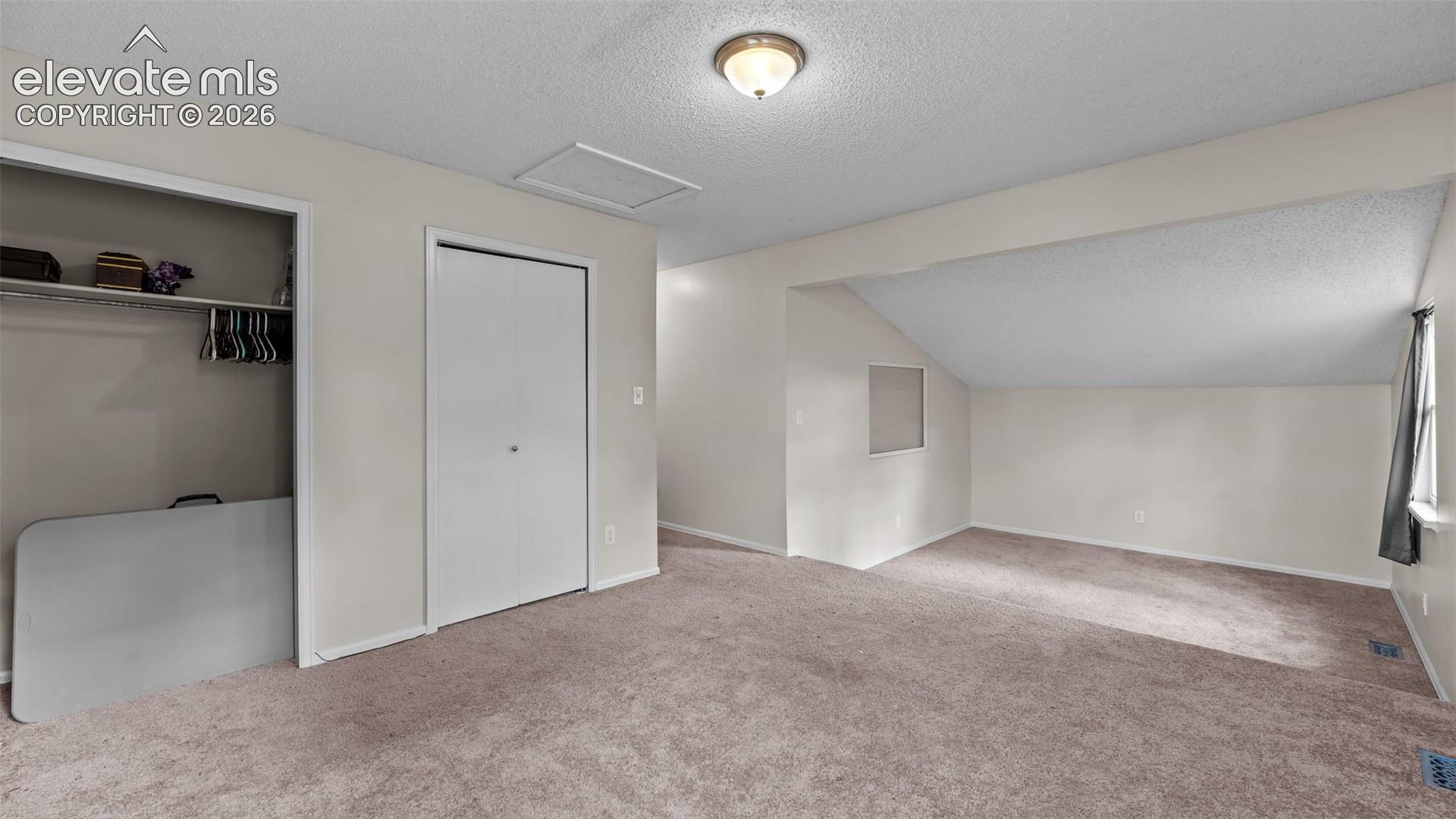 Room featuring wall-to-wall carpeting, sloped ceiling, dual closets with interior shelving, and a flush-mount ceiling light fixture