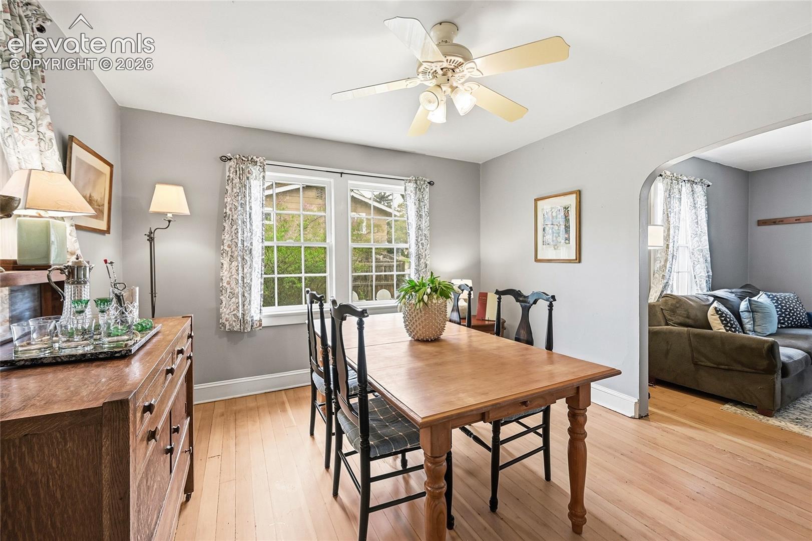 Dining area featuring light-toned wood flooring, a central multi-light ceiling fan, dual multi-pane windows, and a signature arched entry