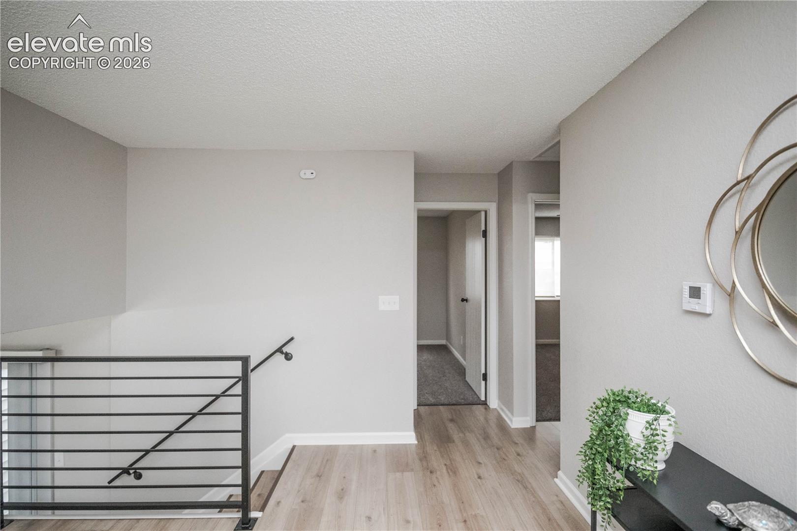 Neutral interior featuring wood-finish flooring, textured ceiling, and a matte black metal stair railing