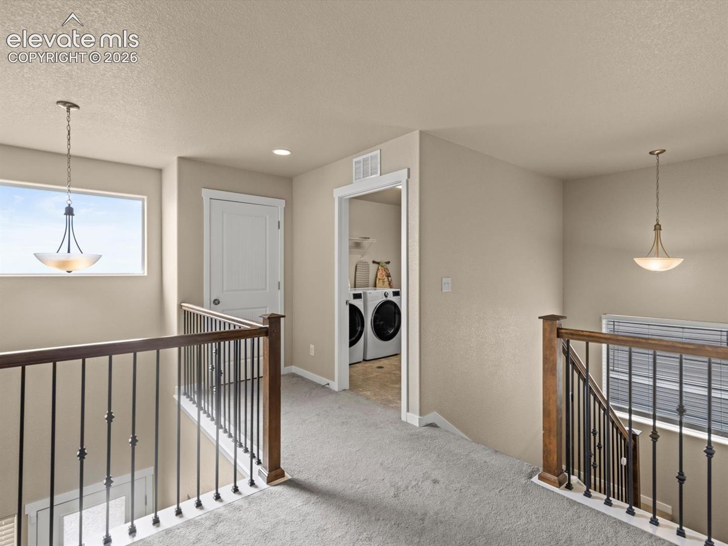 Upper-level landing featuring neutral carpeting, a white paneled door, and dark wood railing with wrought iron balusters