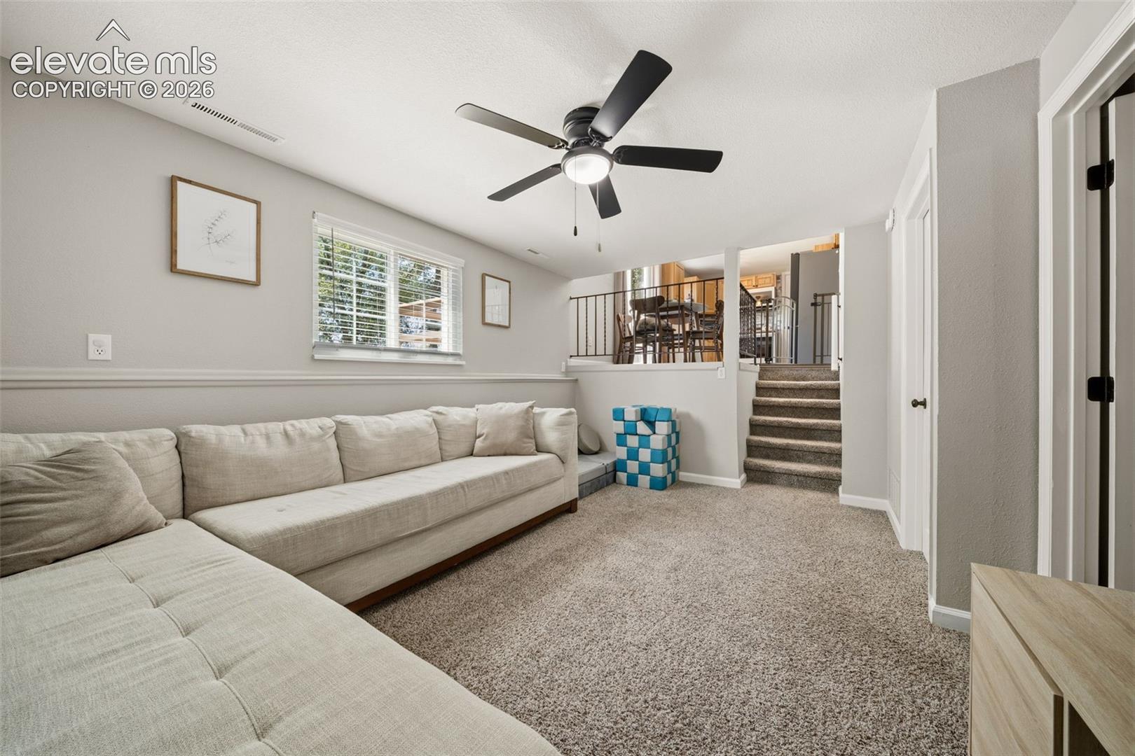 Carpeted lower level featuring a ceiling fan with integrated lighting, a window with blinds, and built-in doors with dark hardware