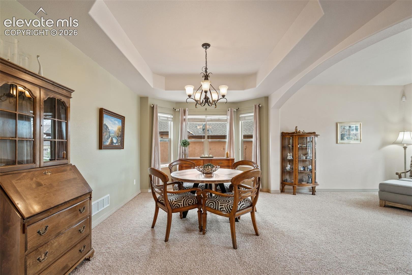 Recessed ceiling with an elegant chandelier, bay window, and arched doorway