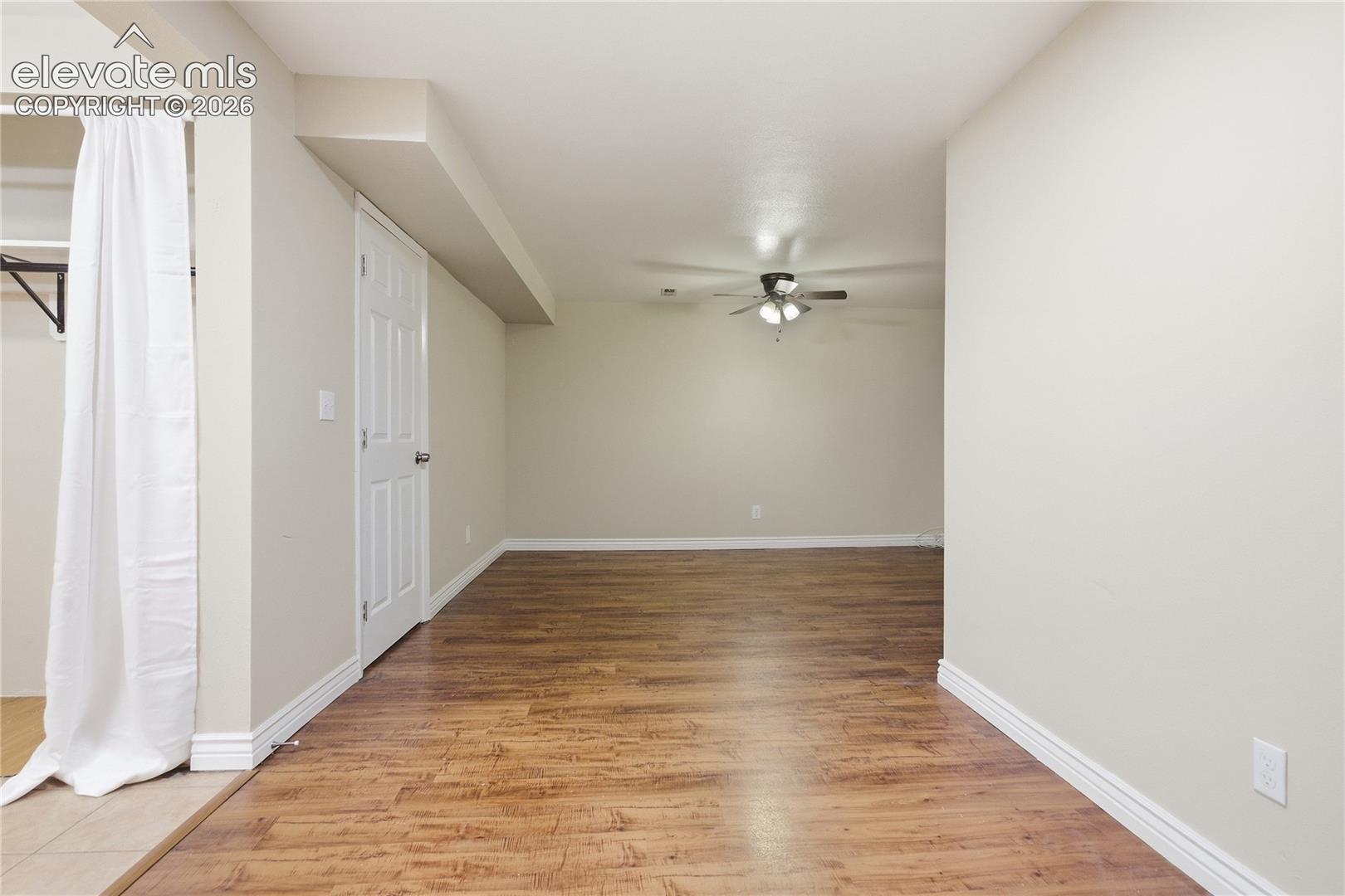 Spacious room featuring wood-finish flooring, light-toned walls, and a ceiling fan