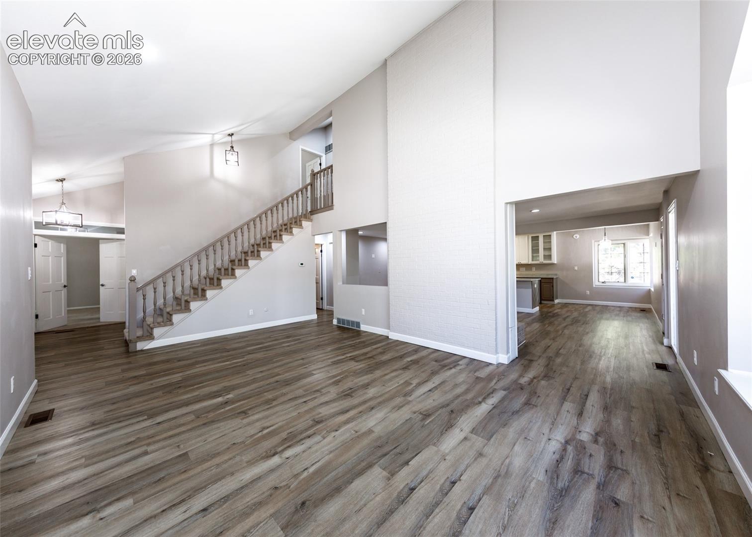 Vaulted ceilings with recessed lighting, wood-finish flooring, a prominent staircase with wood railing, and an open concept layout