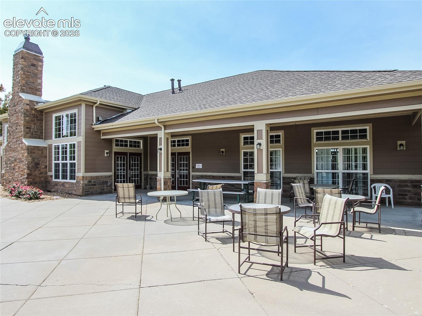 Expansive concrete patio featuring a covered seating area, stone-veneer chimney, and horizontal lap siding