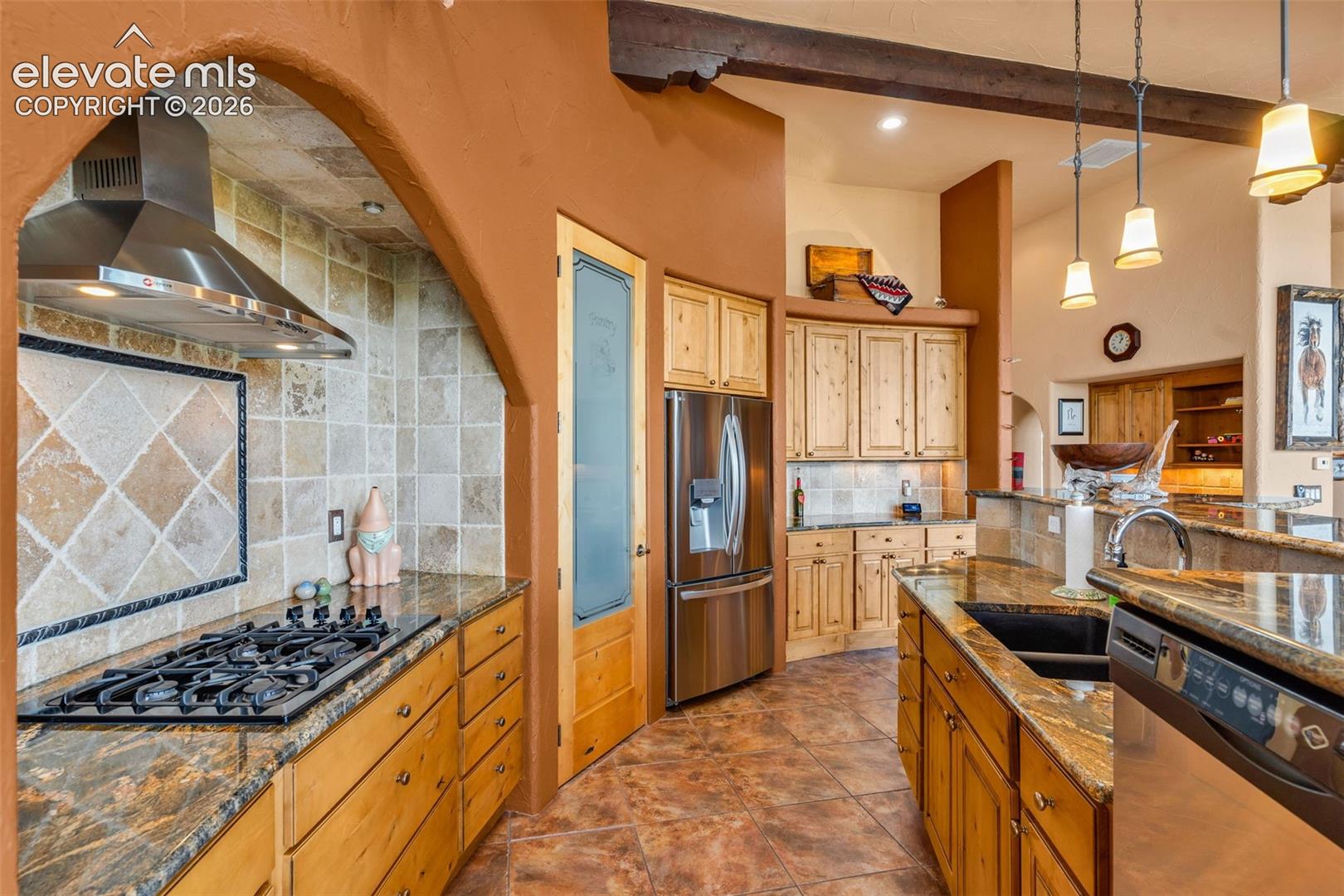 Kitchen featuring natural stone countertops, custom wood cabinetry, stainless steel appliances, stone tile backsplash, and exposed ceiling beams