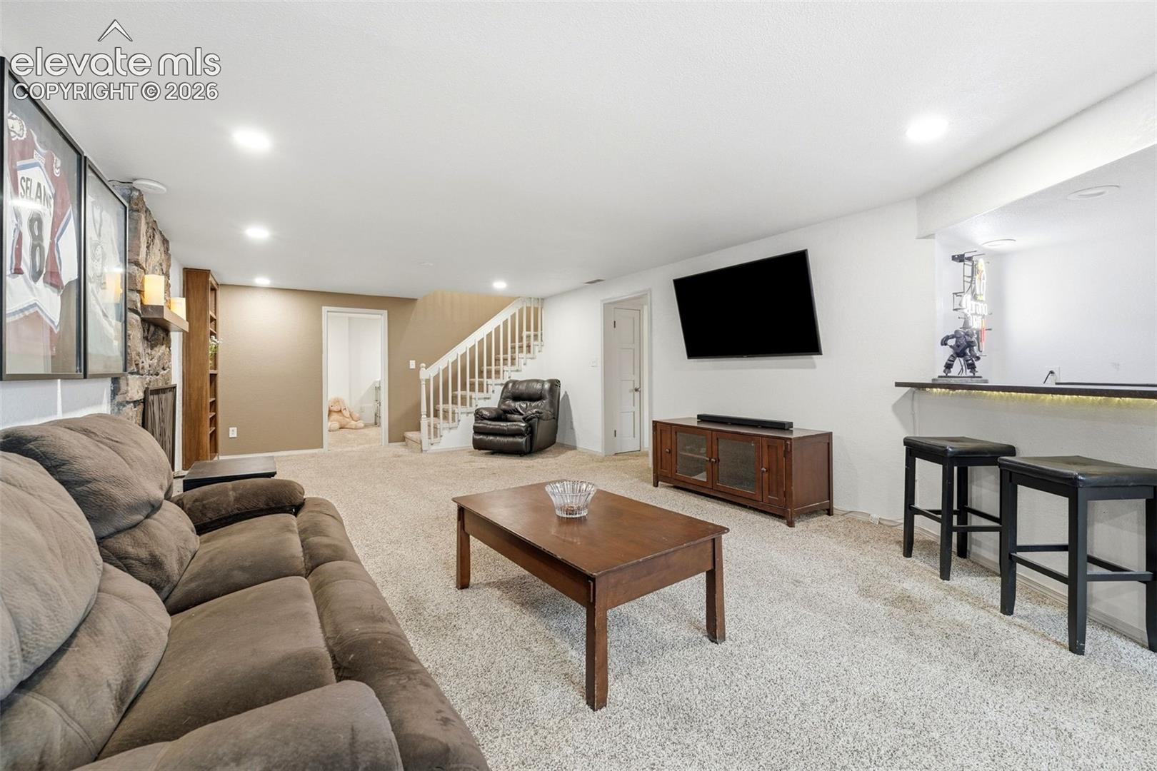 Expansive carpeted recreation room featuring a stone-clad fireplace, built-in shelving, a wet bar with integrated Rec room includes a bar with wet sink and room for an included fridge 