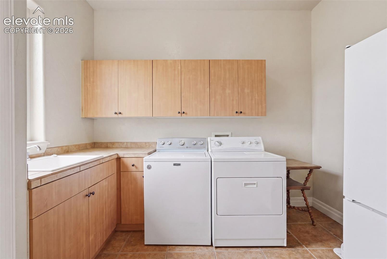 Utility room featuring light wood cabinetry, a built-in sink, and tiled countertops