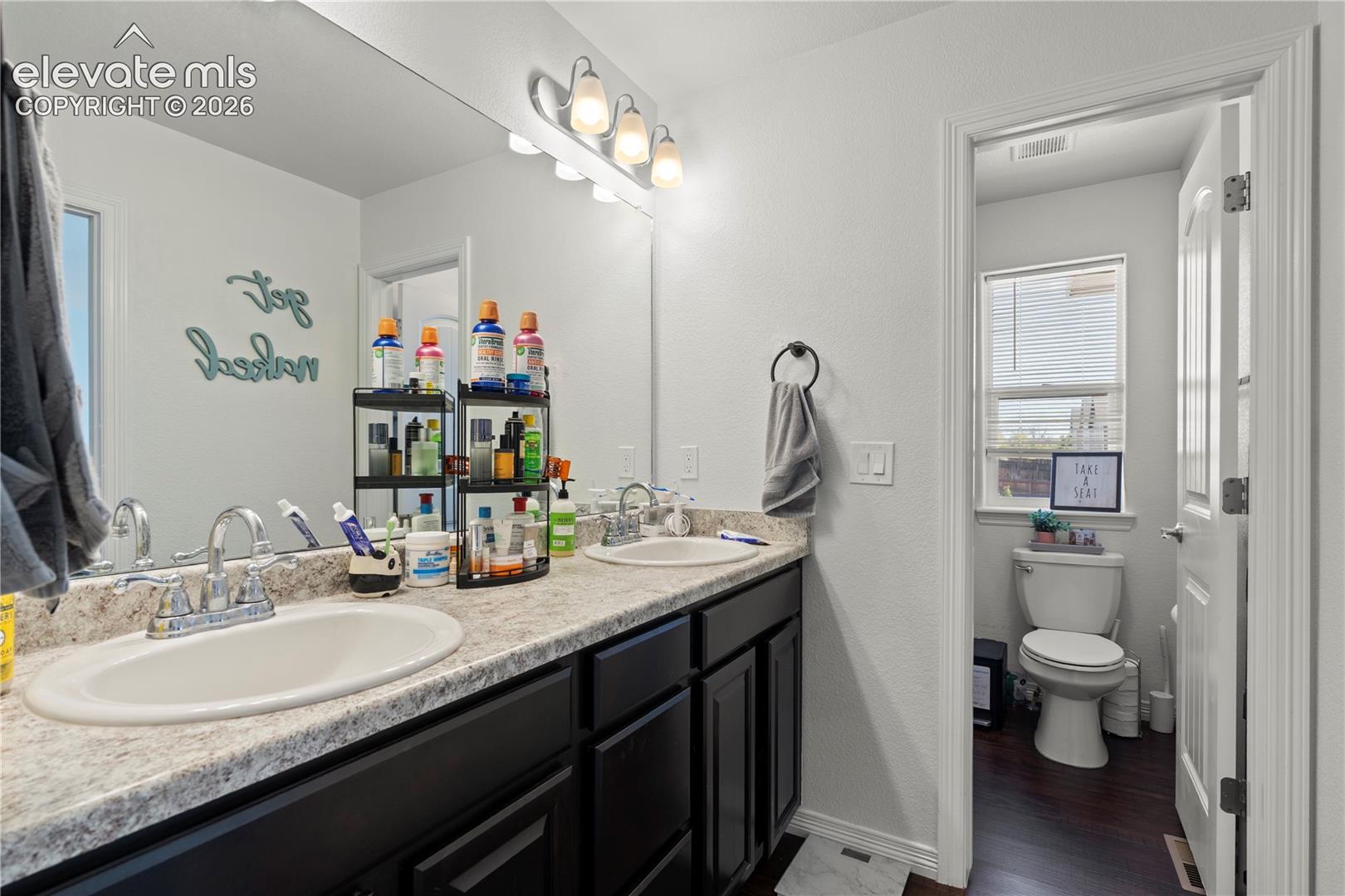 Dual-sink vanity featuring stone-patterned countertops, dark cabinetry, and polished chrome fixtures