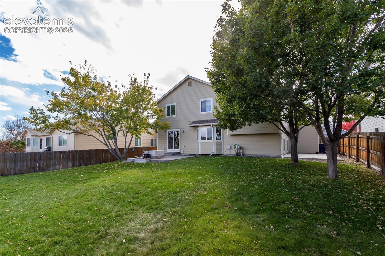Expansive backyard featuring a manicured lawn, mature trees, wood privacy fencing, and two concrete patios