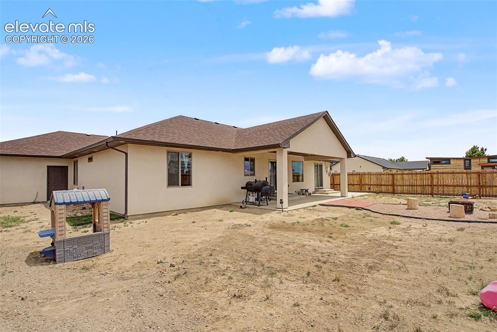 Spacious backyard featuring a covered patio, sliding glass doors, a wood fence, and a fire pit area with stone pavers