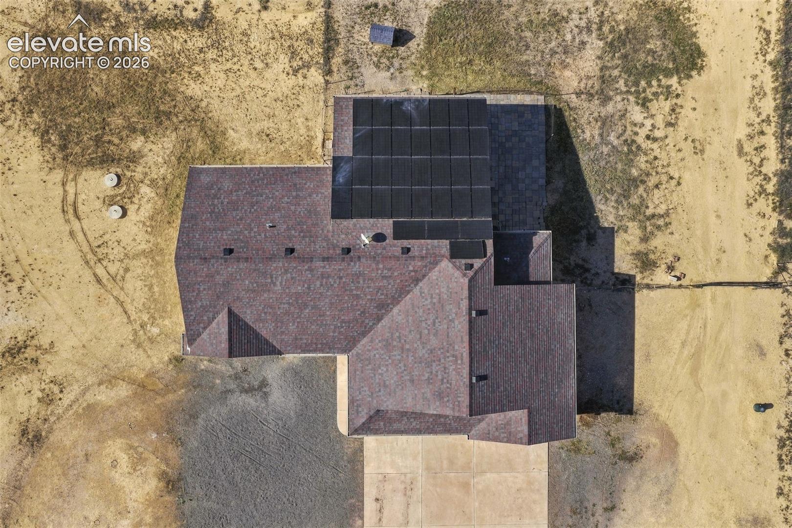 Aerial perspective of the property featuring a composition shingle roof, integrated solar panel array, and concrete driveway