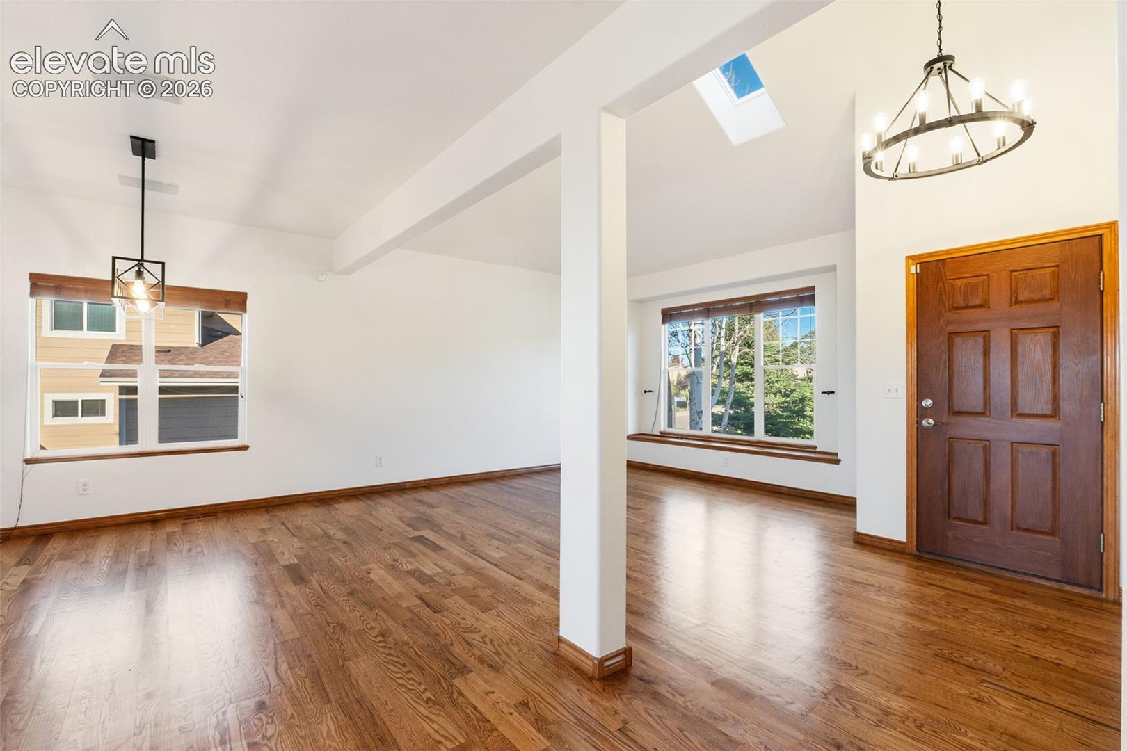 Open-concept interior featuring wood-finish flooring, a vaulted ceiling with a skylight, multi-pane windows, a recessed window seat, and dual industrial-style hanging light fixtures
