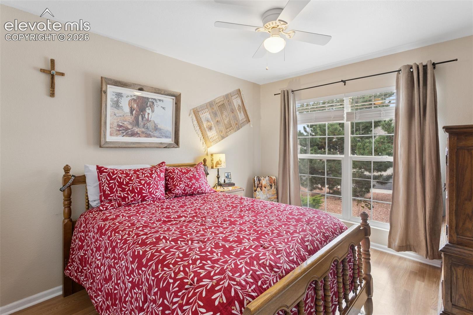 Wood-finish flooring, ceiling fan, and window with exterior landscaping