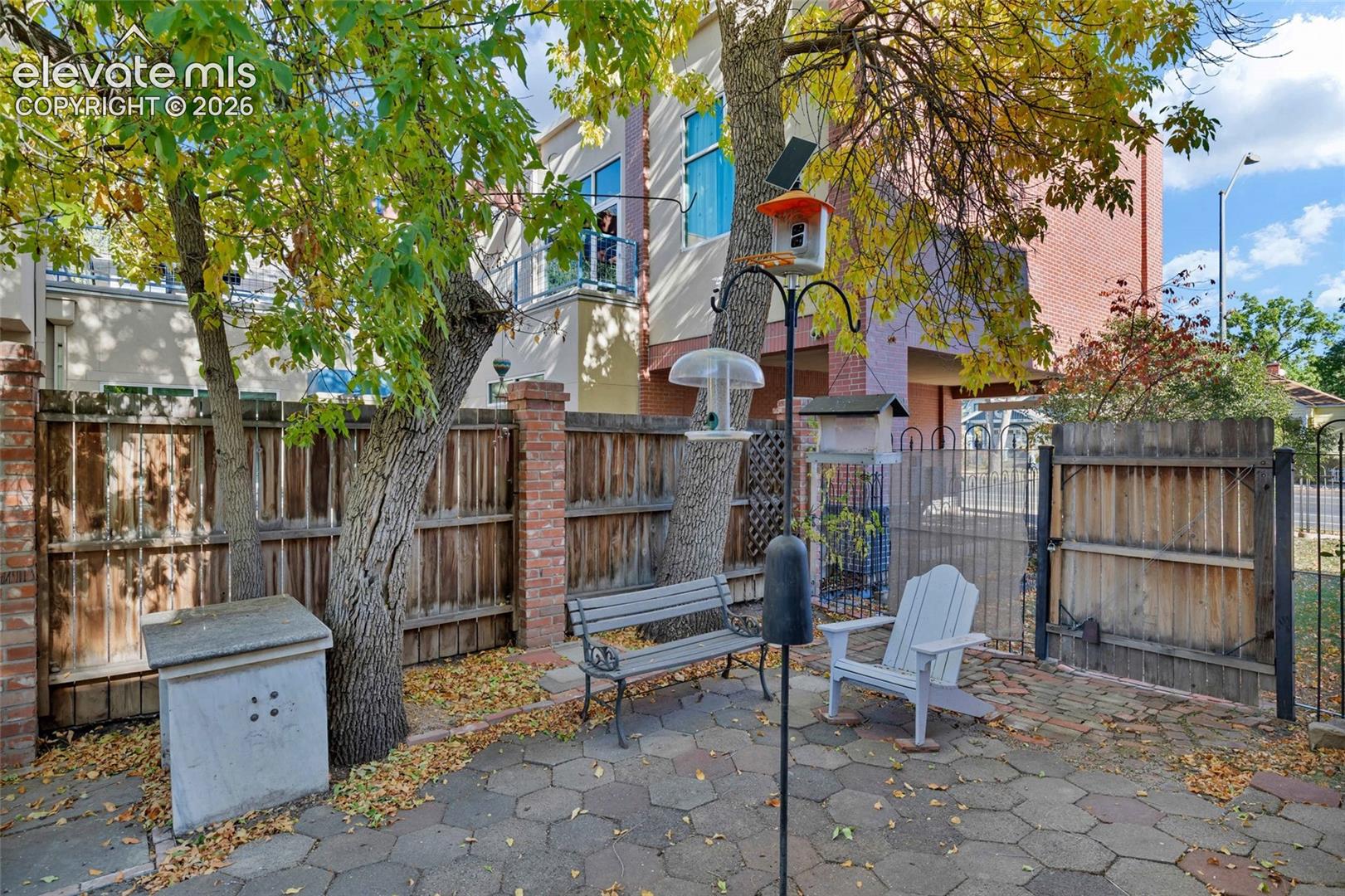 Hexagonal paver patio enclosed by a wood-panel fence with decorative brick pillars and gated access