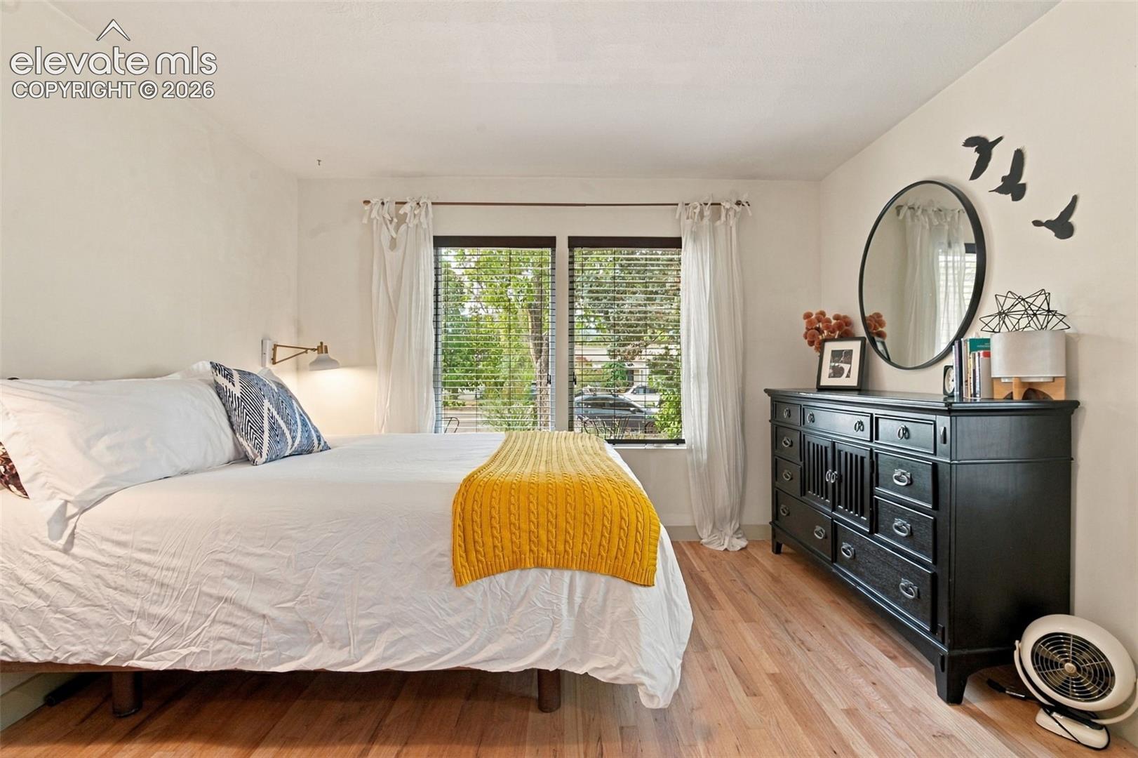 Wood-finish flooring, dual windows with horizontal blinds, and a wall-mounted swing-arm lamp
