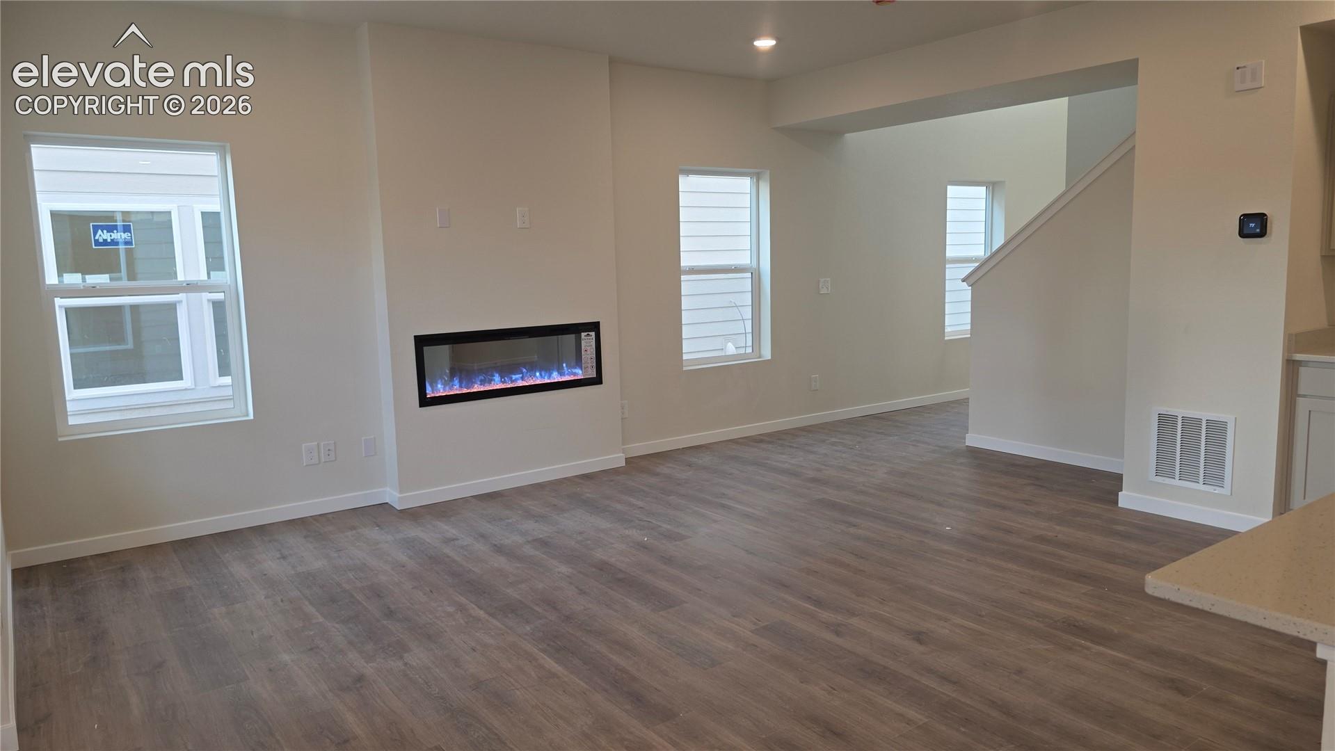 living room with recessed electric fireplace set into a flat wall, two narrow windows and adjacent short stairway half-wall