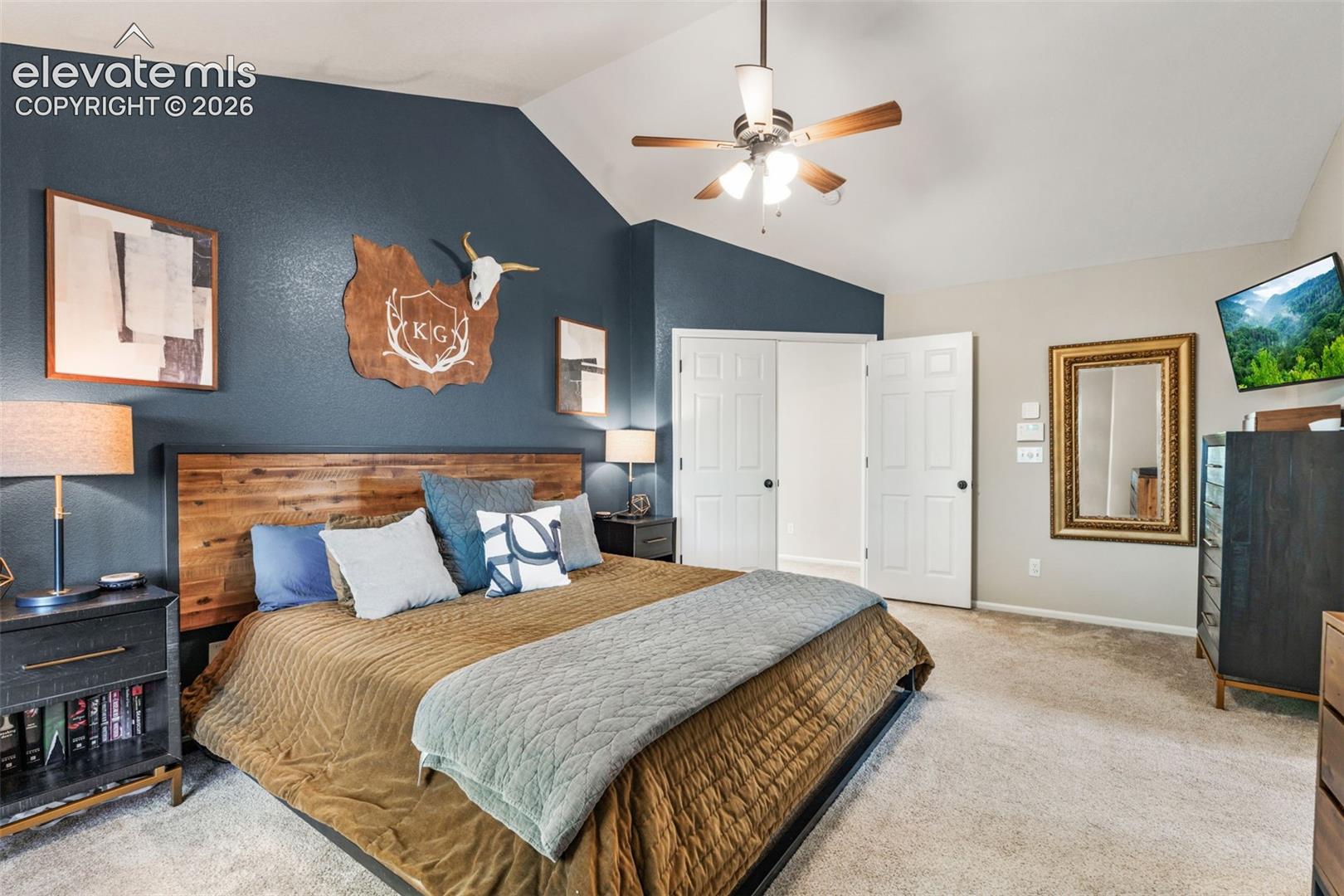 Vaulted ceiling with a central multi-blade ceiling fan, accent wall with a dark blue finish, and neutral carpeting