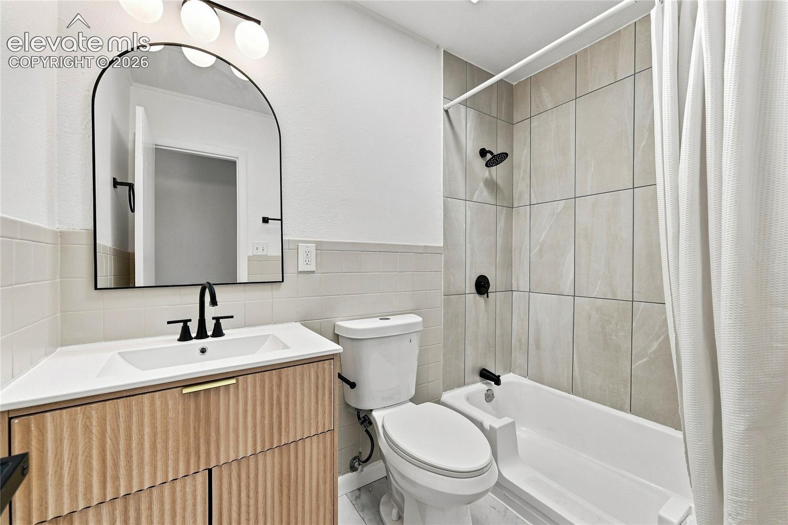 Bathroom featuring a wood-finish vanity with a white countertop, matte black fixtures, an arched mirror, and a tiled shower/tub combination