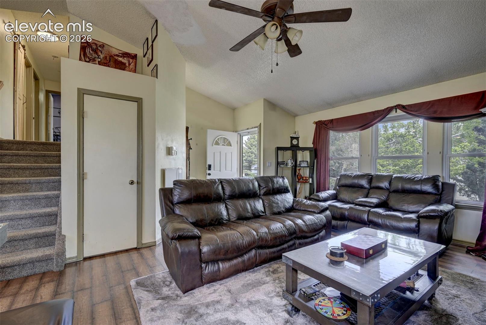 Living area featuring wood-finish flooring, vaulted ceilings, and a ceiling fan with integrated lighting
