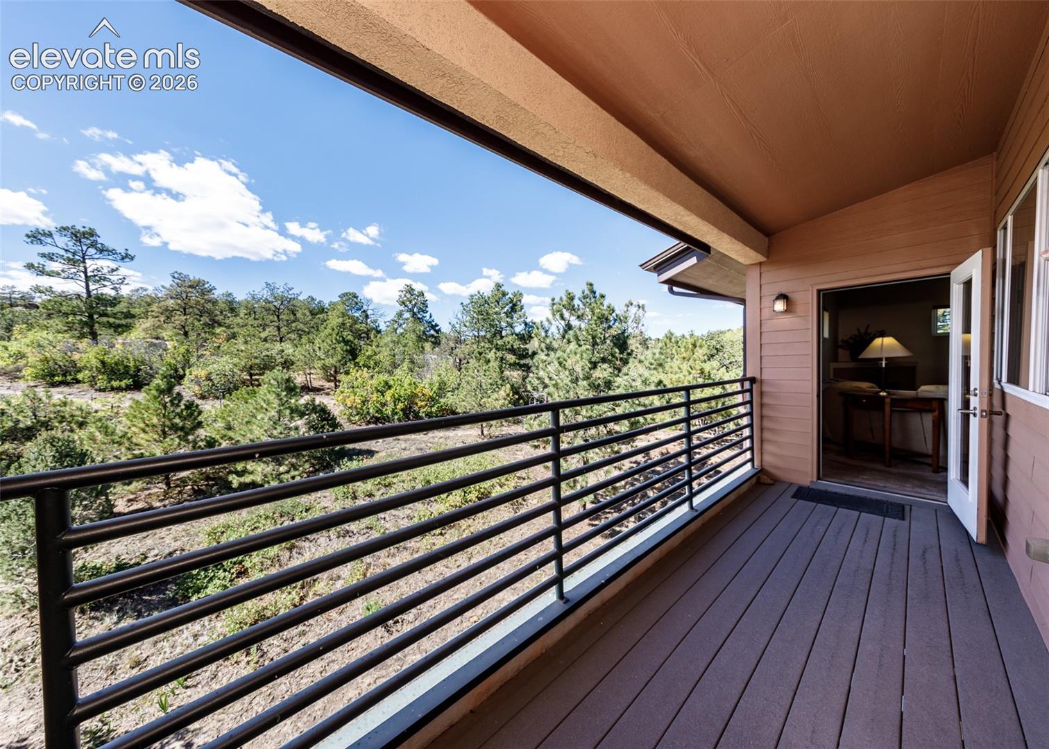 Covered balcony featuring composite decking, horizontal metal railing, and exterior wall-mounted lighting