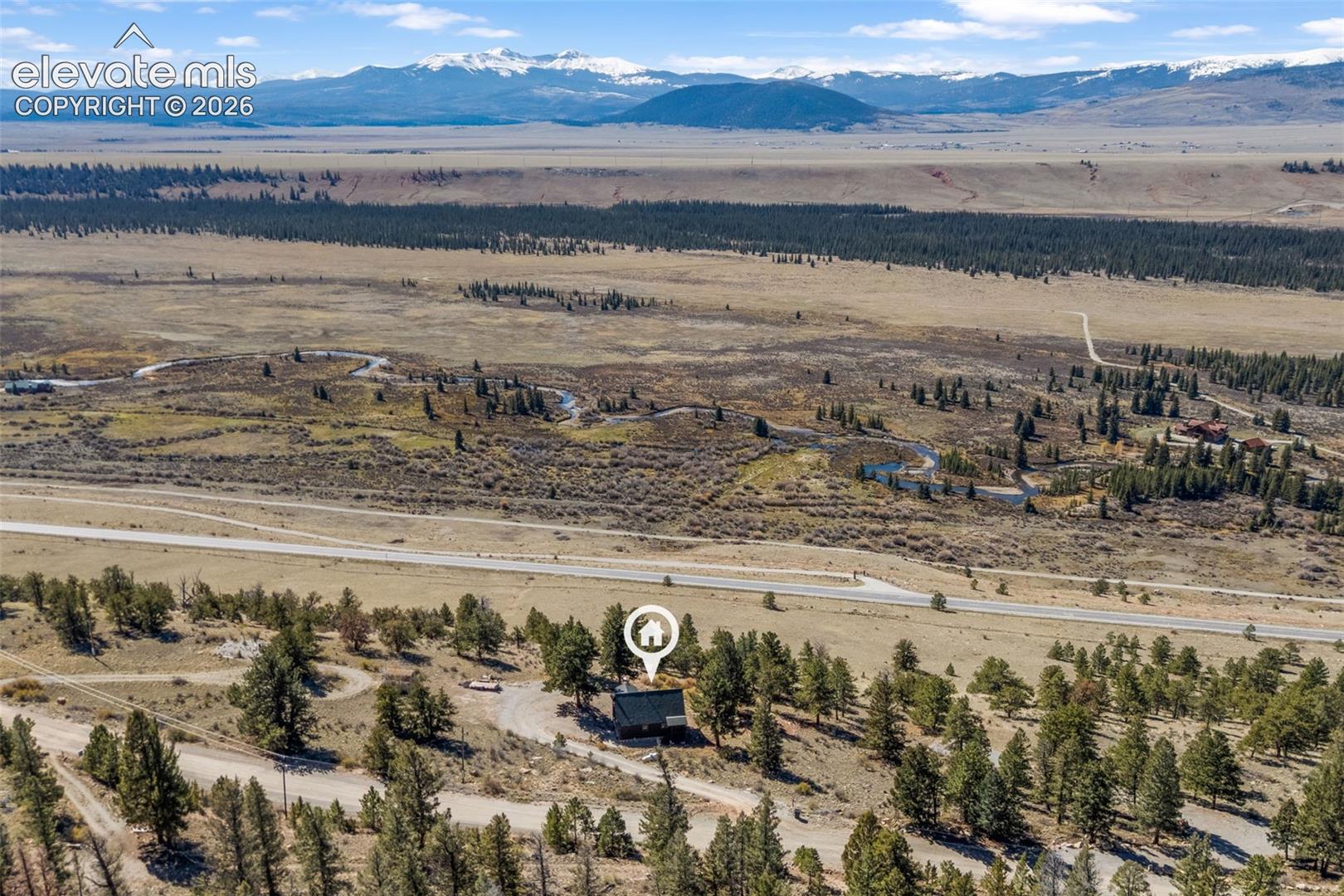 Aerial perspective featuring expansive acreage, mature evergreen trees, and a mountain range backdrop