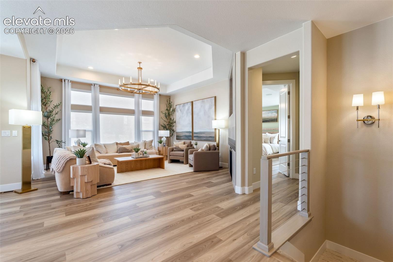 Tray ceiling with a central chandelier, wood-finish flooring, extensive multi-pane window configuration, and metal cable railing
