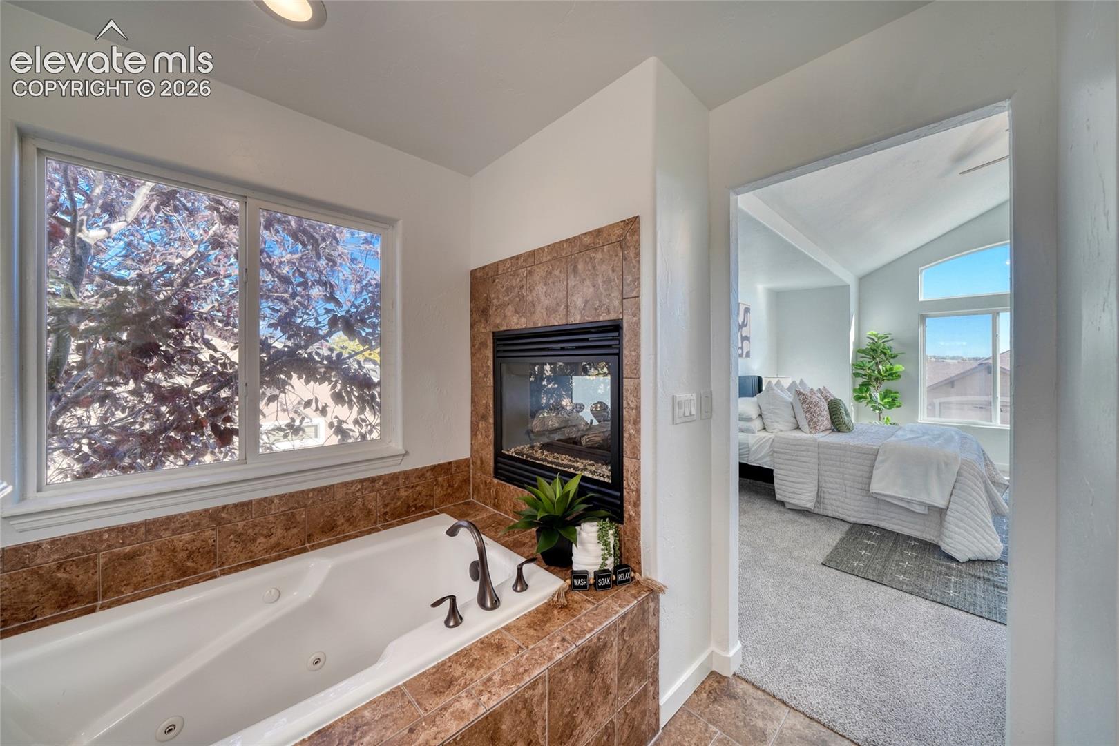 Jetted soaking tub with tile surround, built-in fireplace, and a window