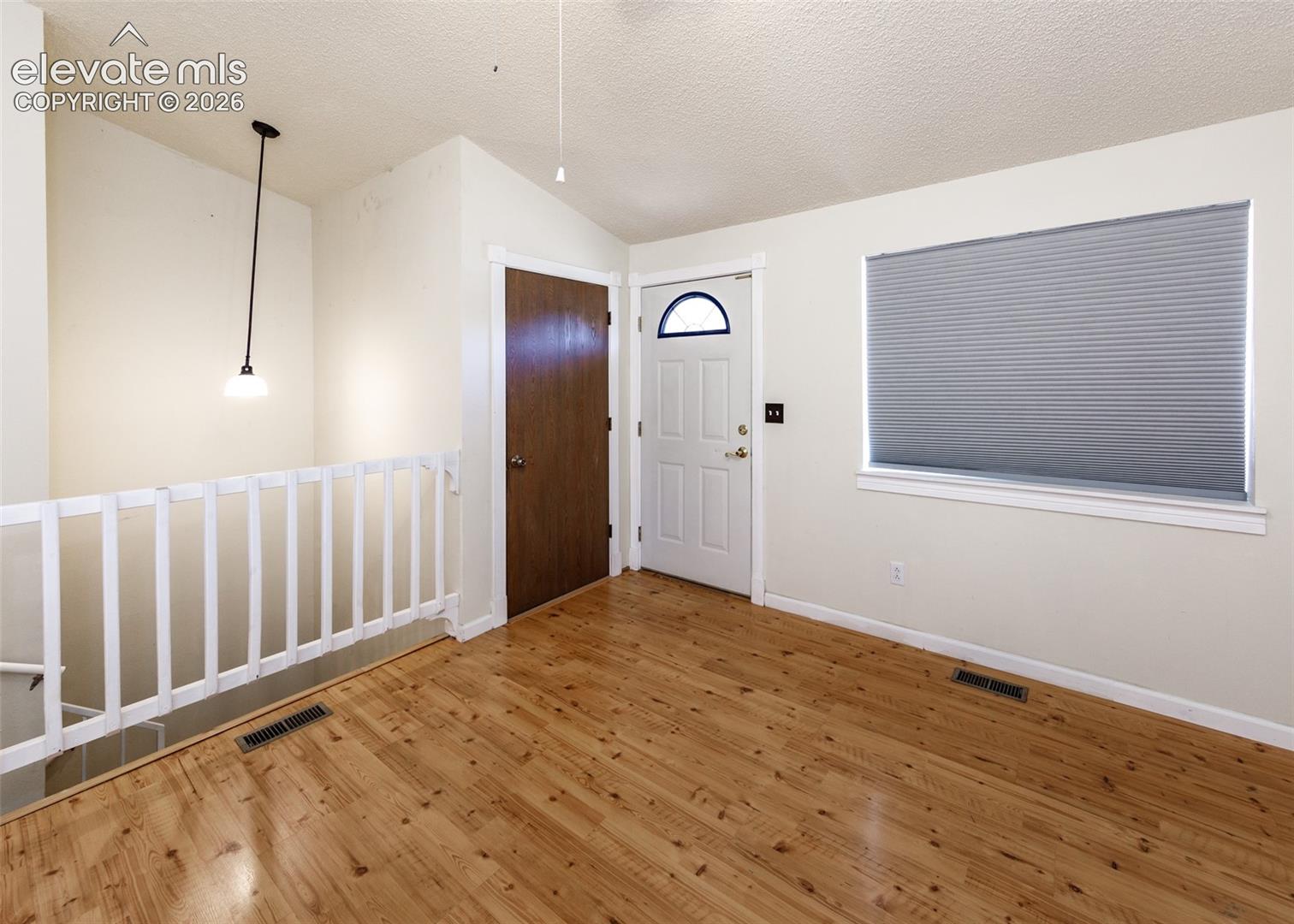 Wood-finish flooring, white railing, pendant lighting, and a paneled exterior door with a decorative glass insert