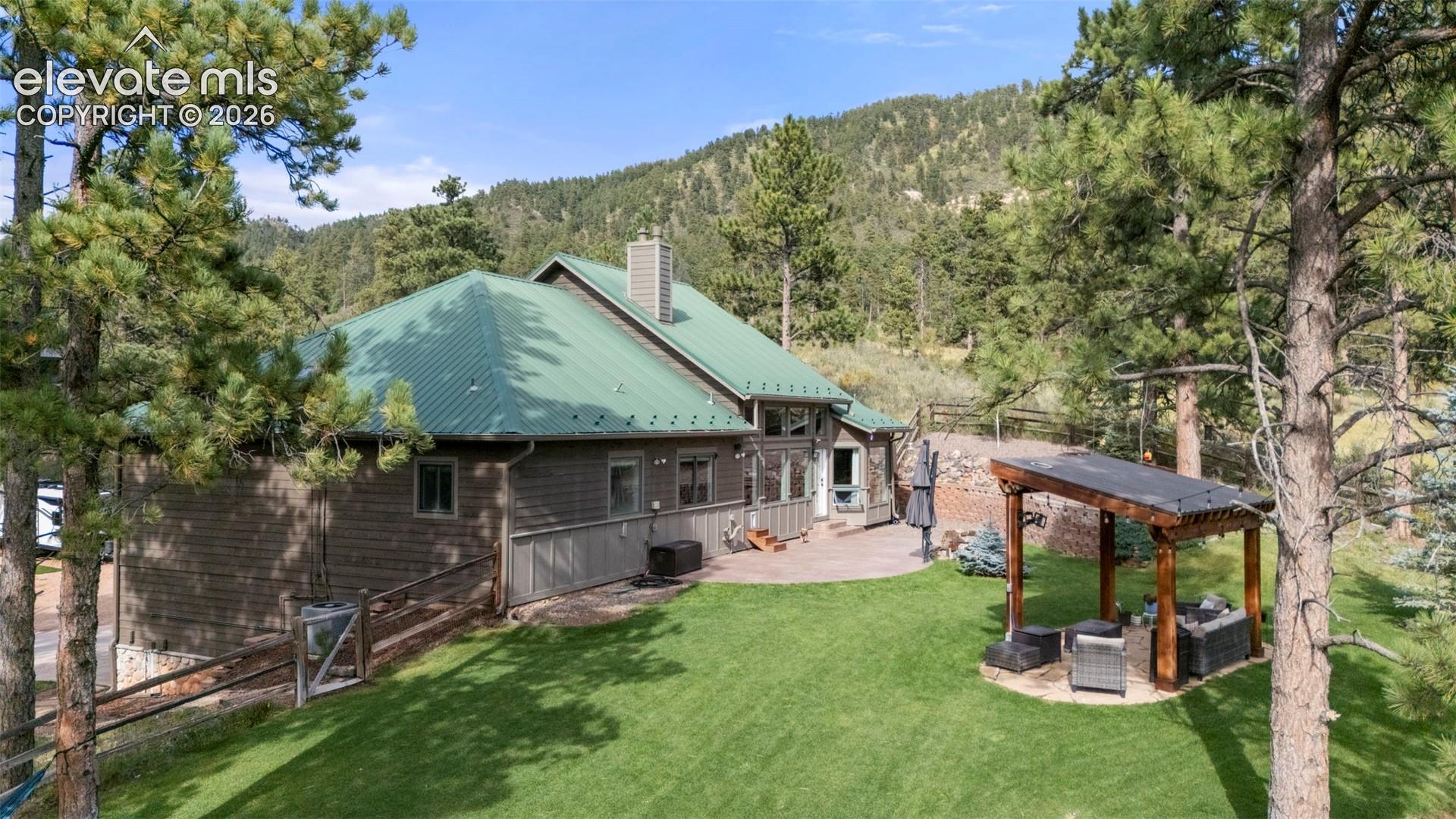 Back of property featuring a patio area, a wooded view, a metal roof, an outdoor hangout area, and a chimney
