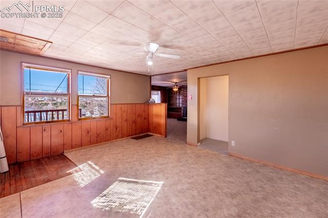Unfurnished room featuring wooden walls, ceiling fan, a wainscoted wall, and light carpet