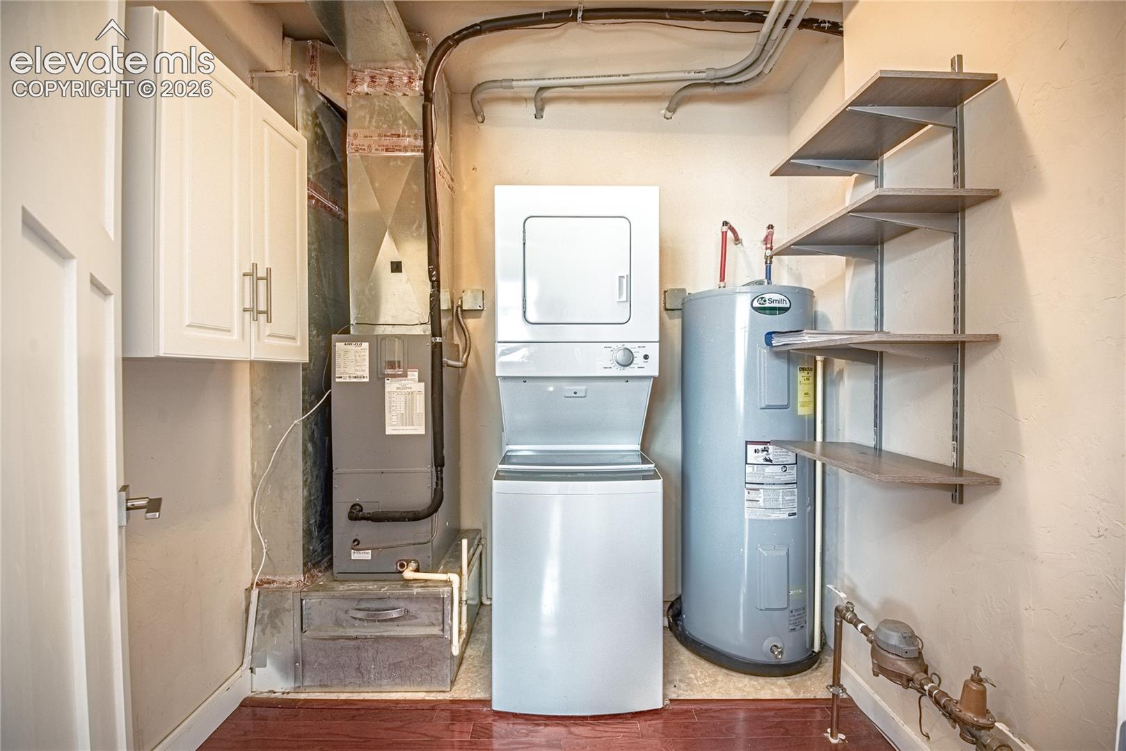 Dedicated utility area featuring a stackable washer and dryer, water heater, and built-in wall shelving