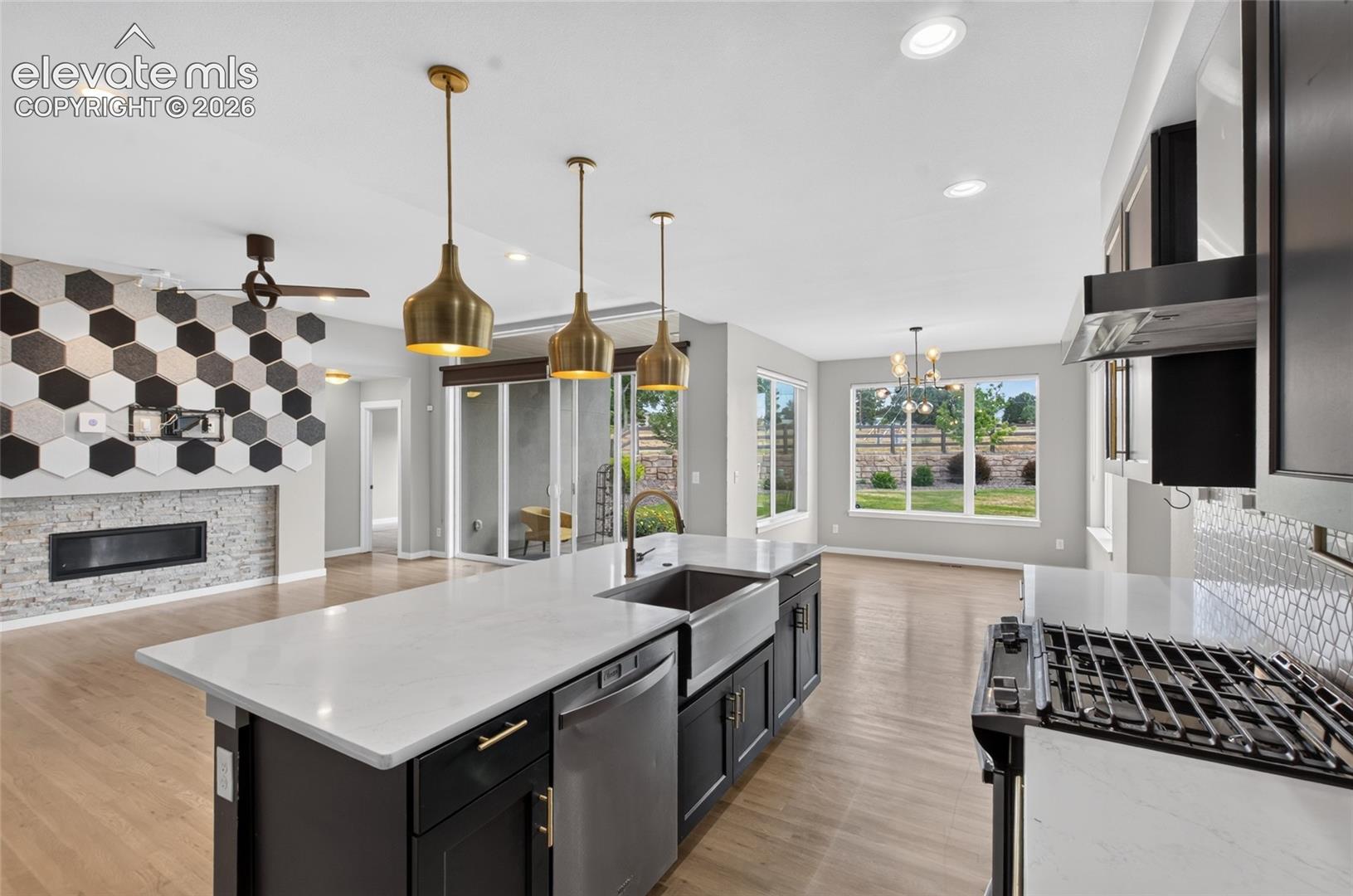 Open-concept kitchen with a large island featuring a farmhouse sink, stainless steel dishwasher, and brass pendant lighting