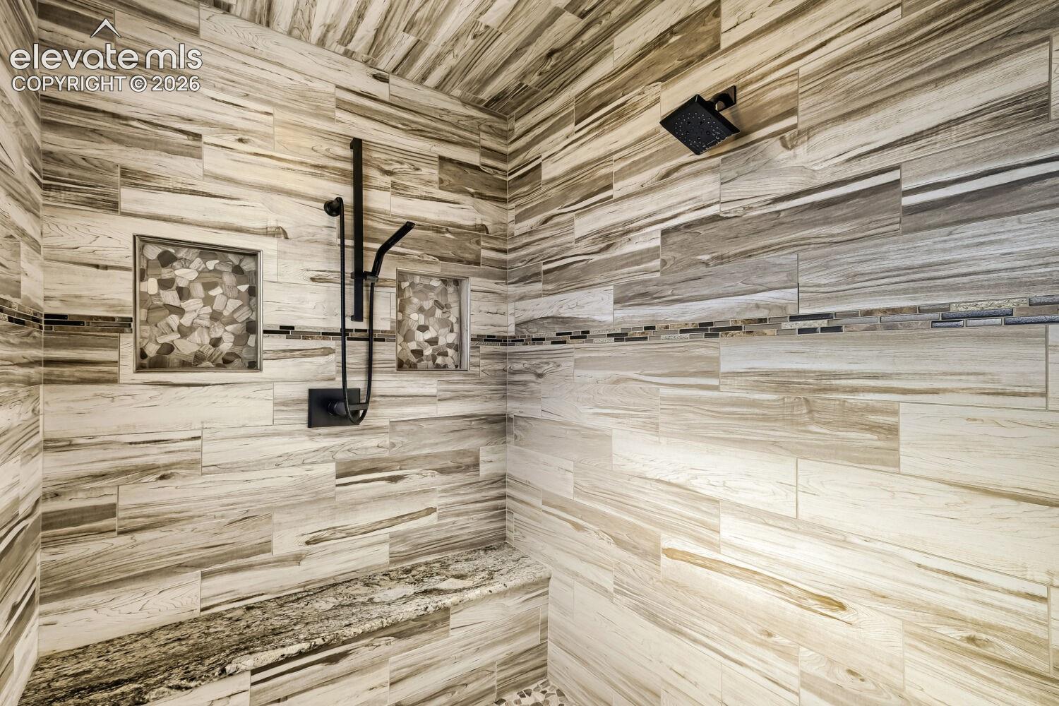 Tiled shower with a rainfall showerhead, handheld shower fixture, built-in bench, and two recessed niches