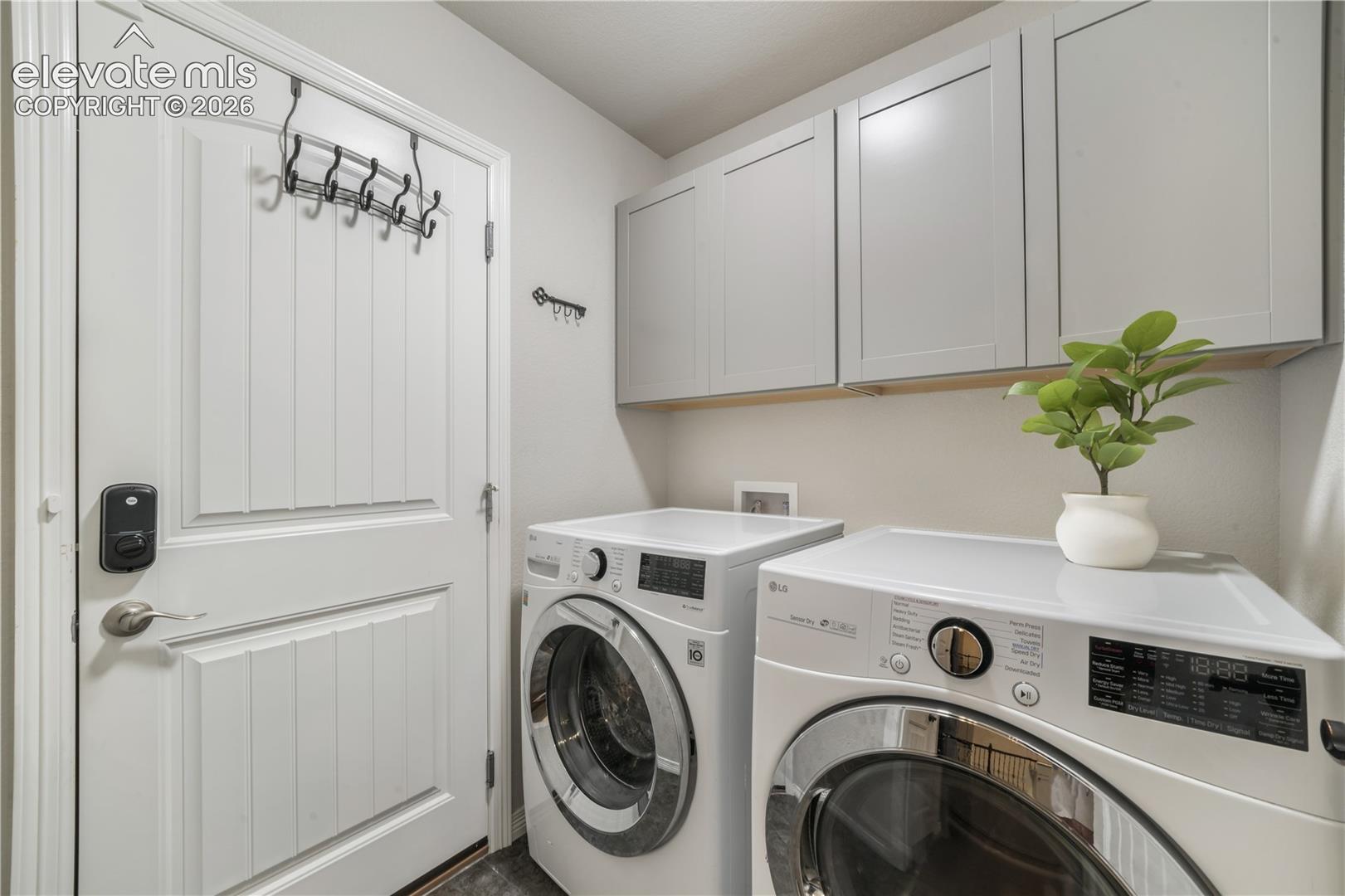 White paneled door with smart lock, overhead cabinetry with light wood accent, and dark flooring