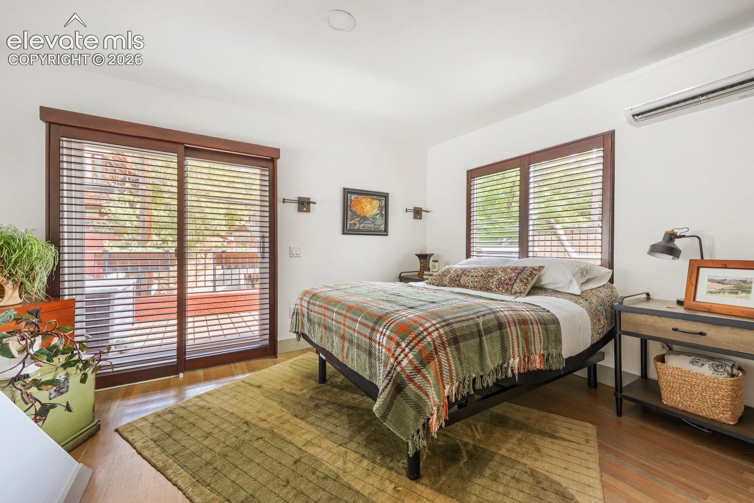 Hardwood flooring, sliding glass door with horizontal blinds, built-in wall sconces, ceiling-mounted lighting, and a wall-mounted air conditioning unit