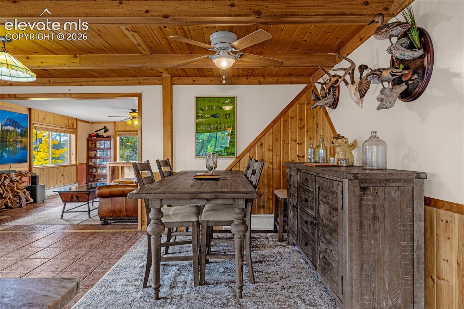Exposed wood beam ceiling featuring integrated wood paneling, tile flooring, and a ceiling fan with light fixture