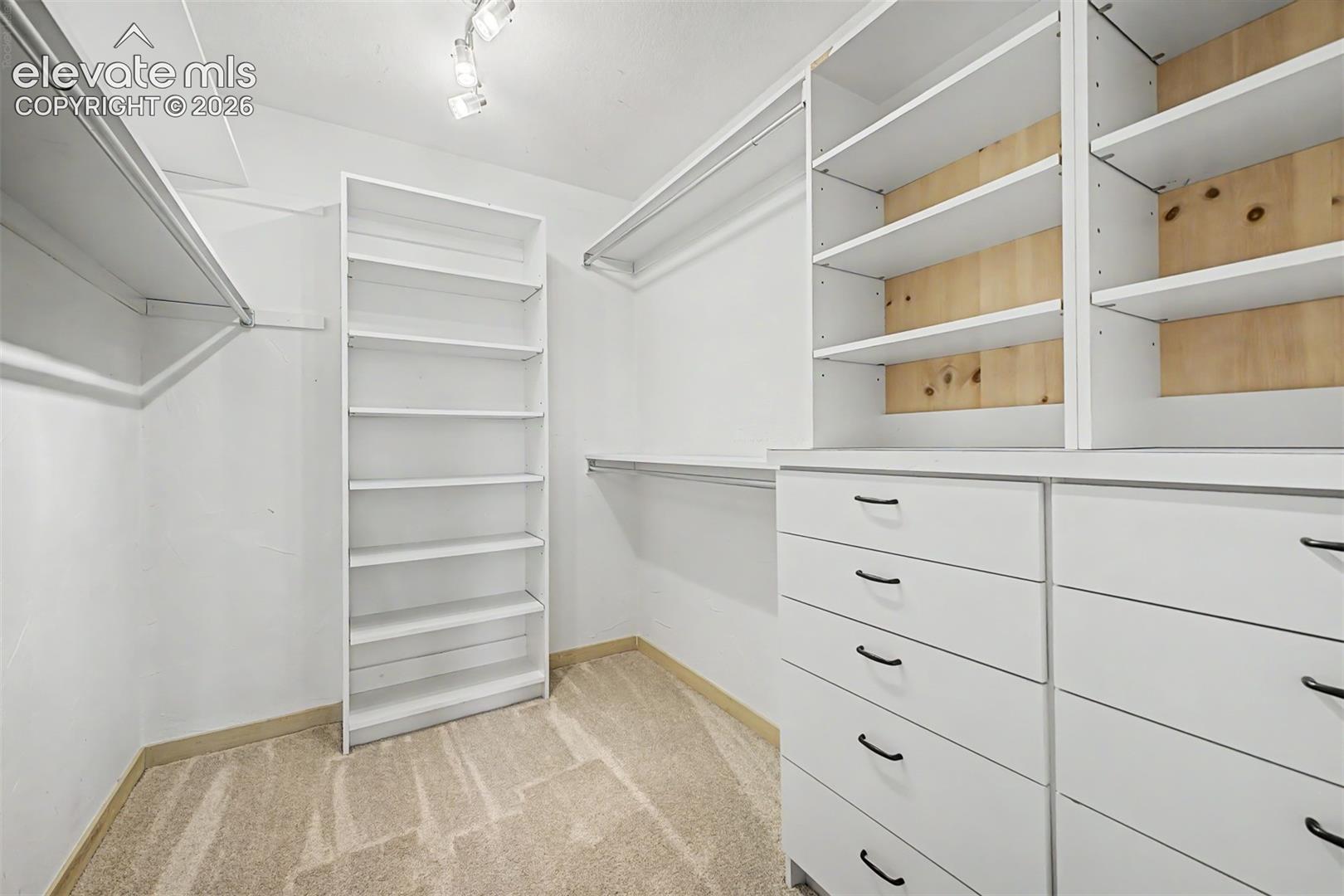 Walk-in closet featuring built-in shelving, integrated drawers, and track lighting