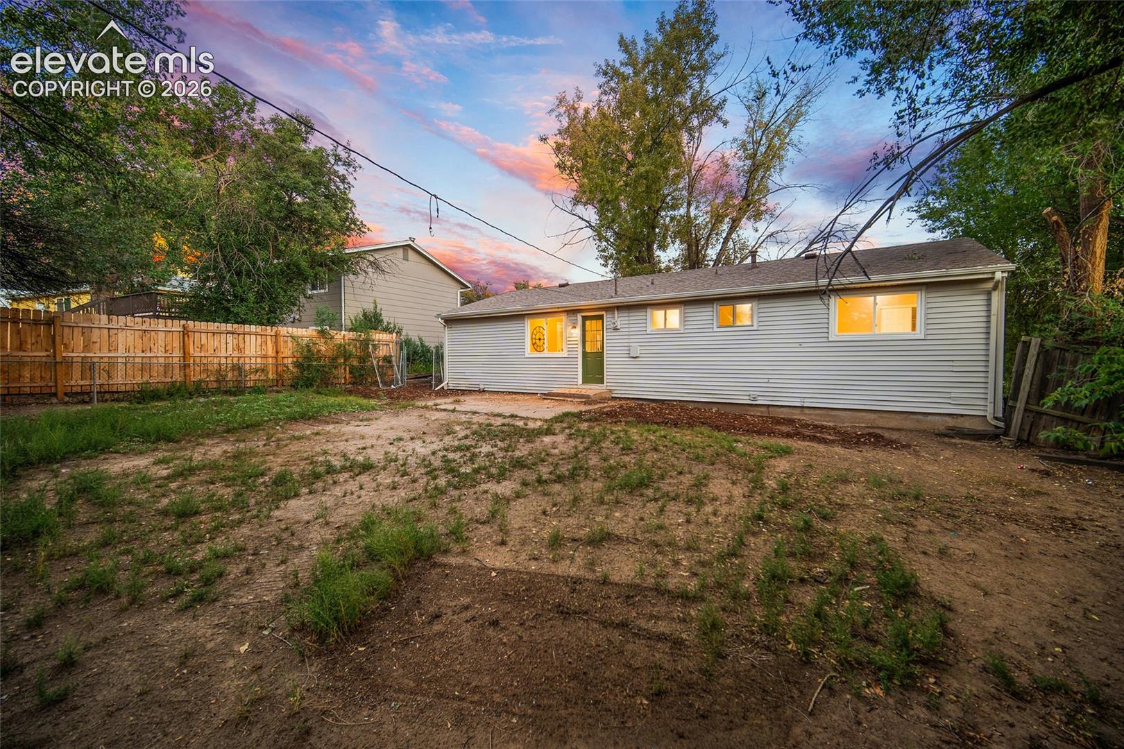 Rear exterior featuring horizontal siding, multiple windows, a green entry door, and a concrete patio