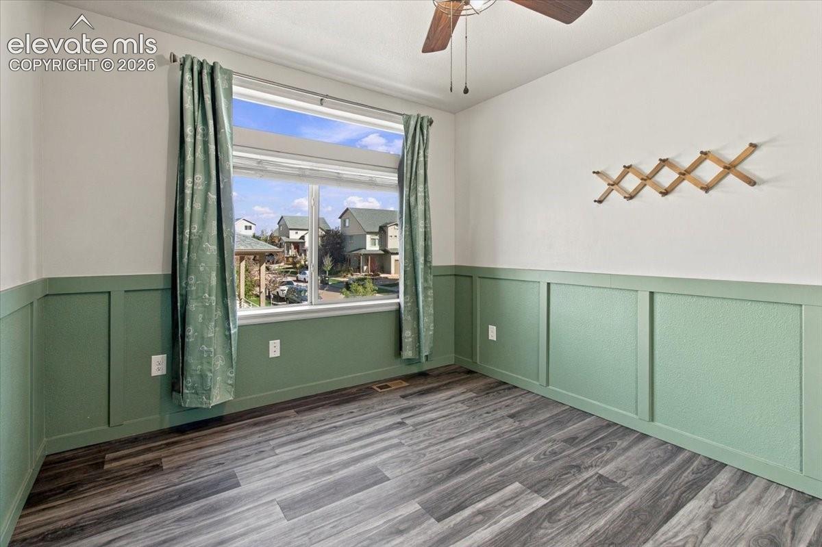 Wood-finish flooring, half-wall wainscoting, and a ceiling fan with integrated lighting