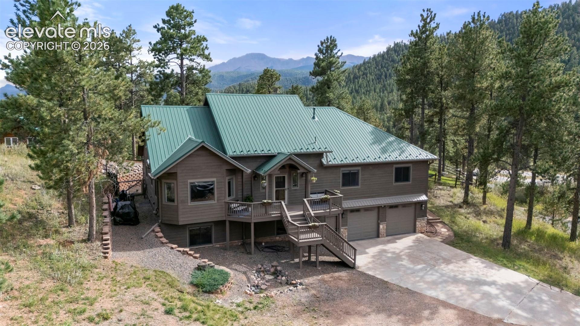 View of front facade with stairway, a deck with mountain view, a metal roof, concrete driveway, and a garage