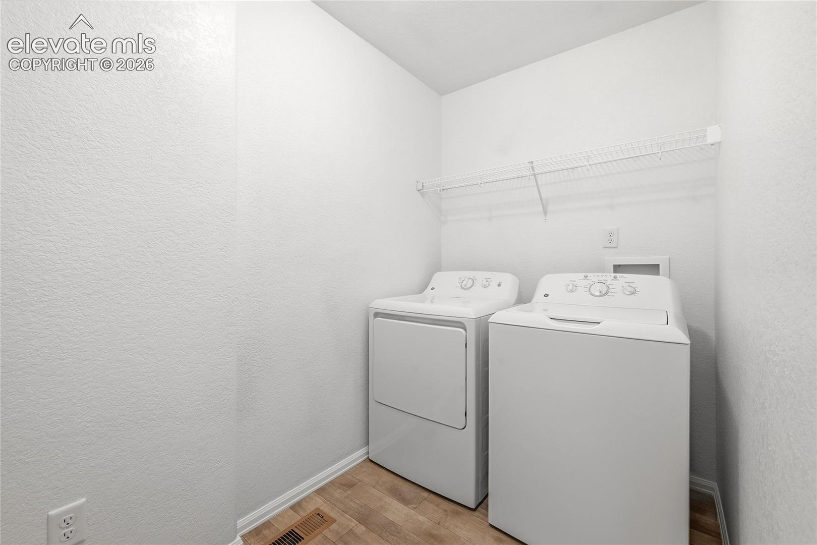 Laundry area featuring white top-load washer and dryer, wood-finish flooring, and wall-mounted wire shelving
