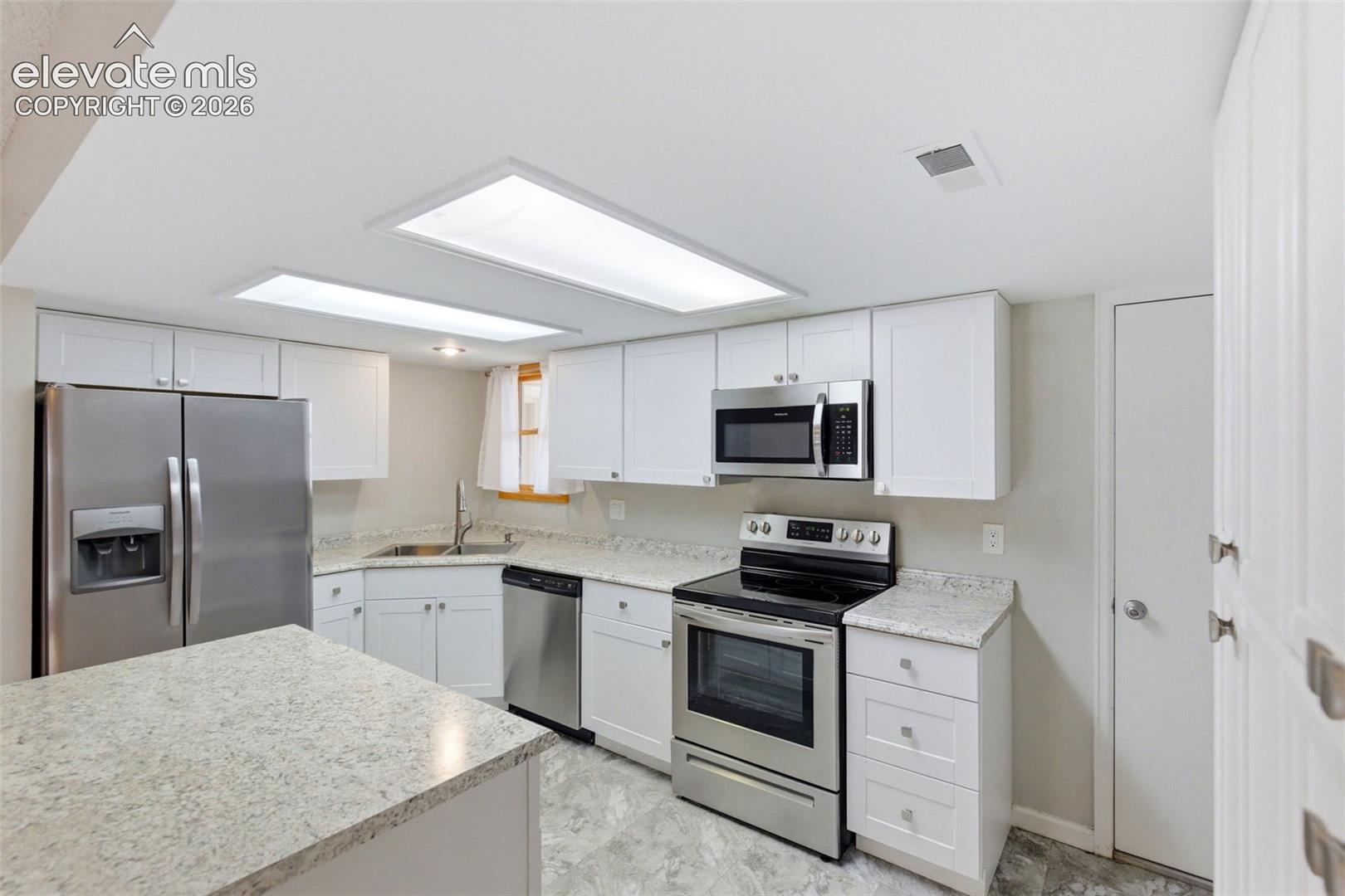 Kitchen featuring stainless steel appliances, white cabinetry, light-toned countertops, and two rectangular ceiling lights