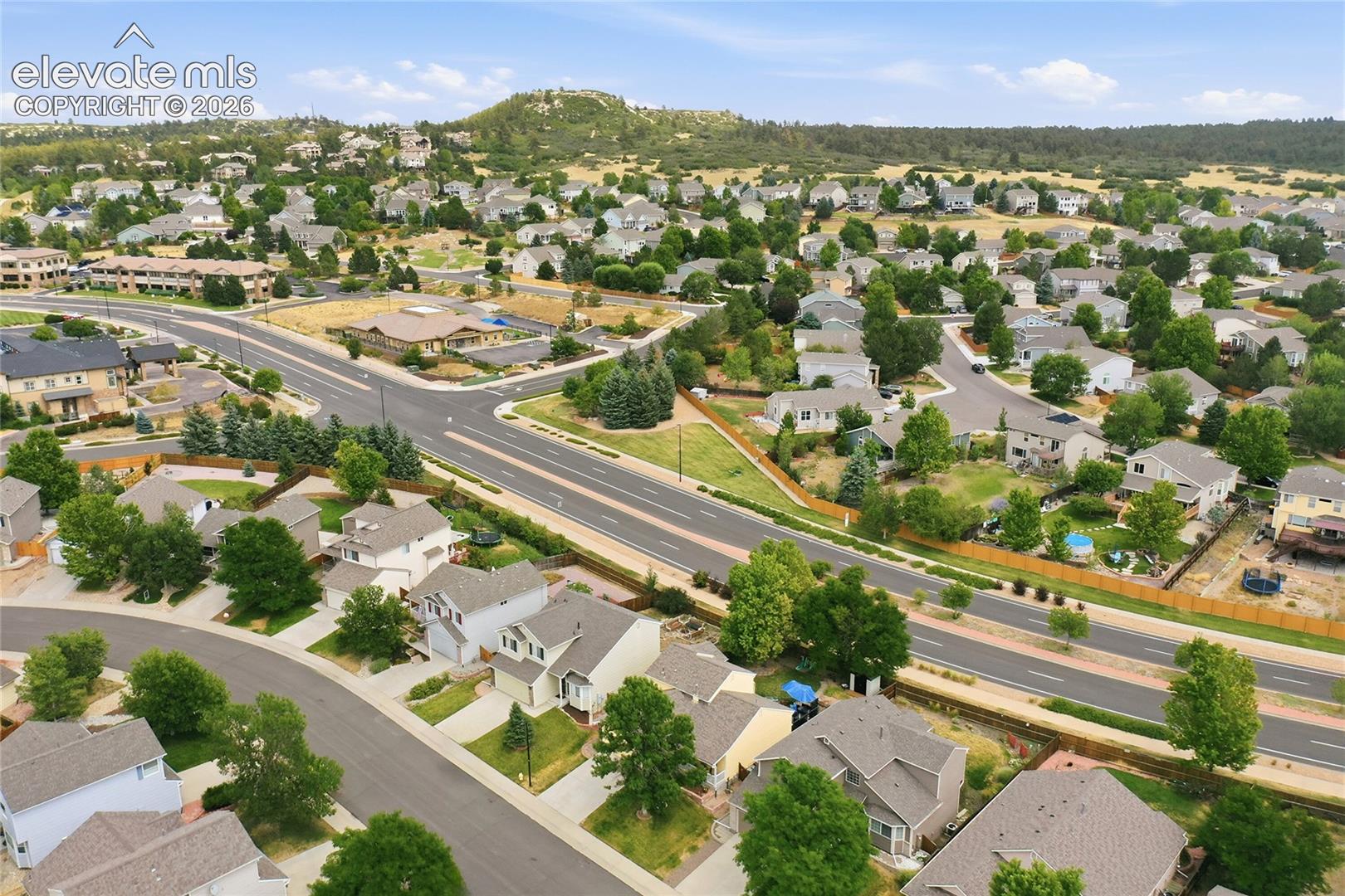 Aerial perspective of a suburban neighborhood featuring paved street infrastructure, mature tree canopy, varied architectural styles, and prominent hilly terrain backdrop