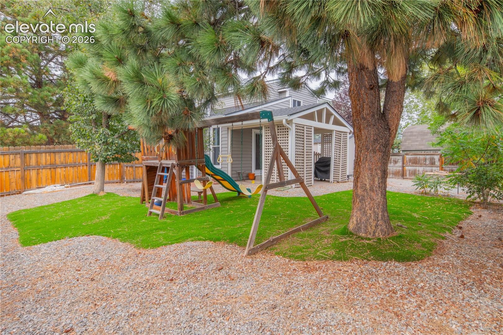 Backyard featuring a covered patio, a privacy trellis, an artificial turf area, and mature trees