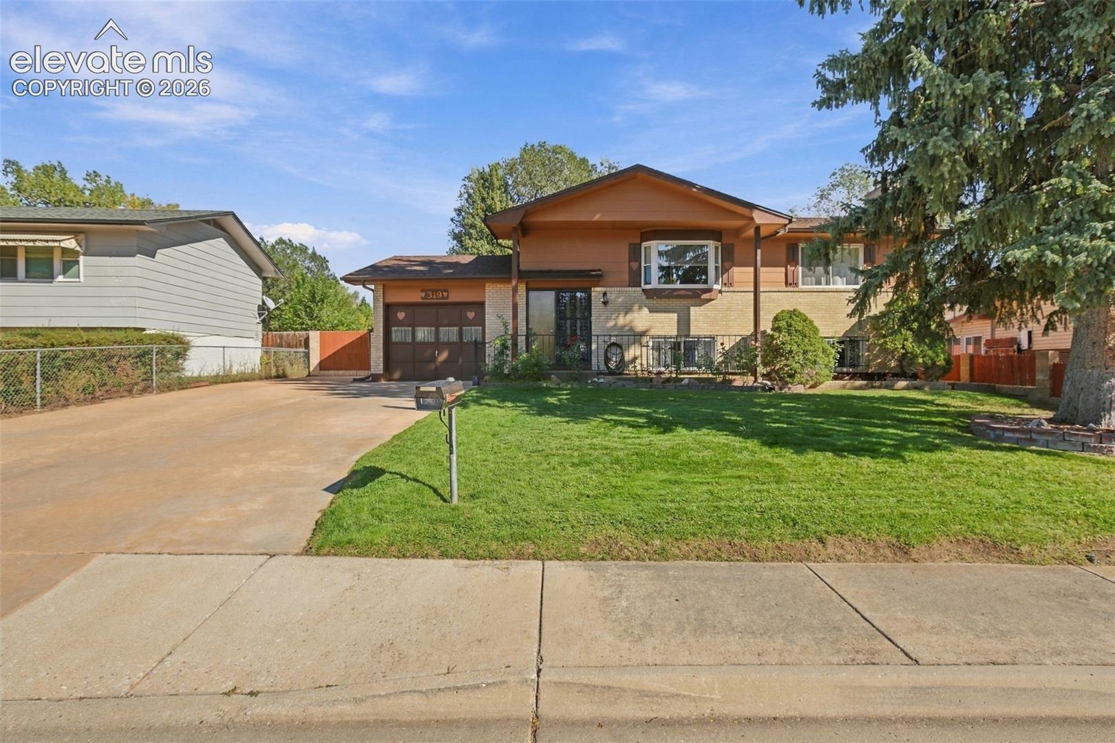 Split-level exterior featuring a combination of brick and wood-paneled siding, a prominent bay window, an attached single-car garage with wood-style door, and a concrete driveway