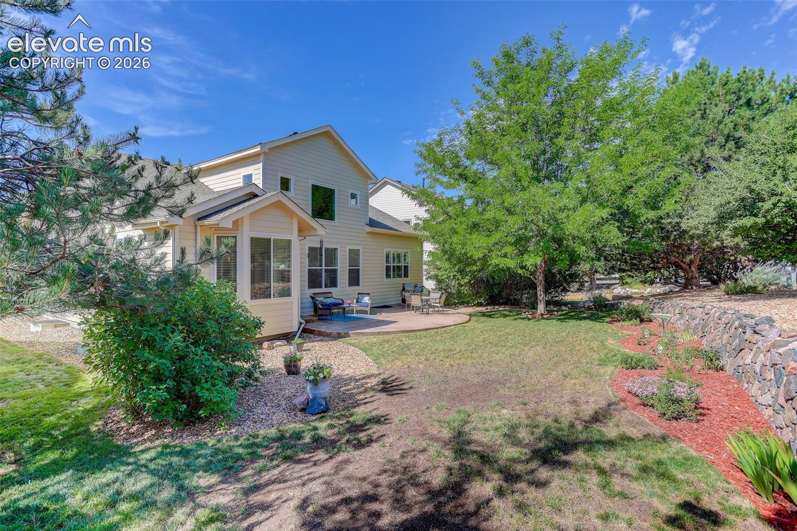 Spacious backyard with a curved paver patio, a screened-in porch, mature trees, and a rock wall